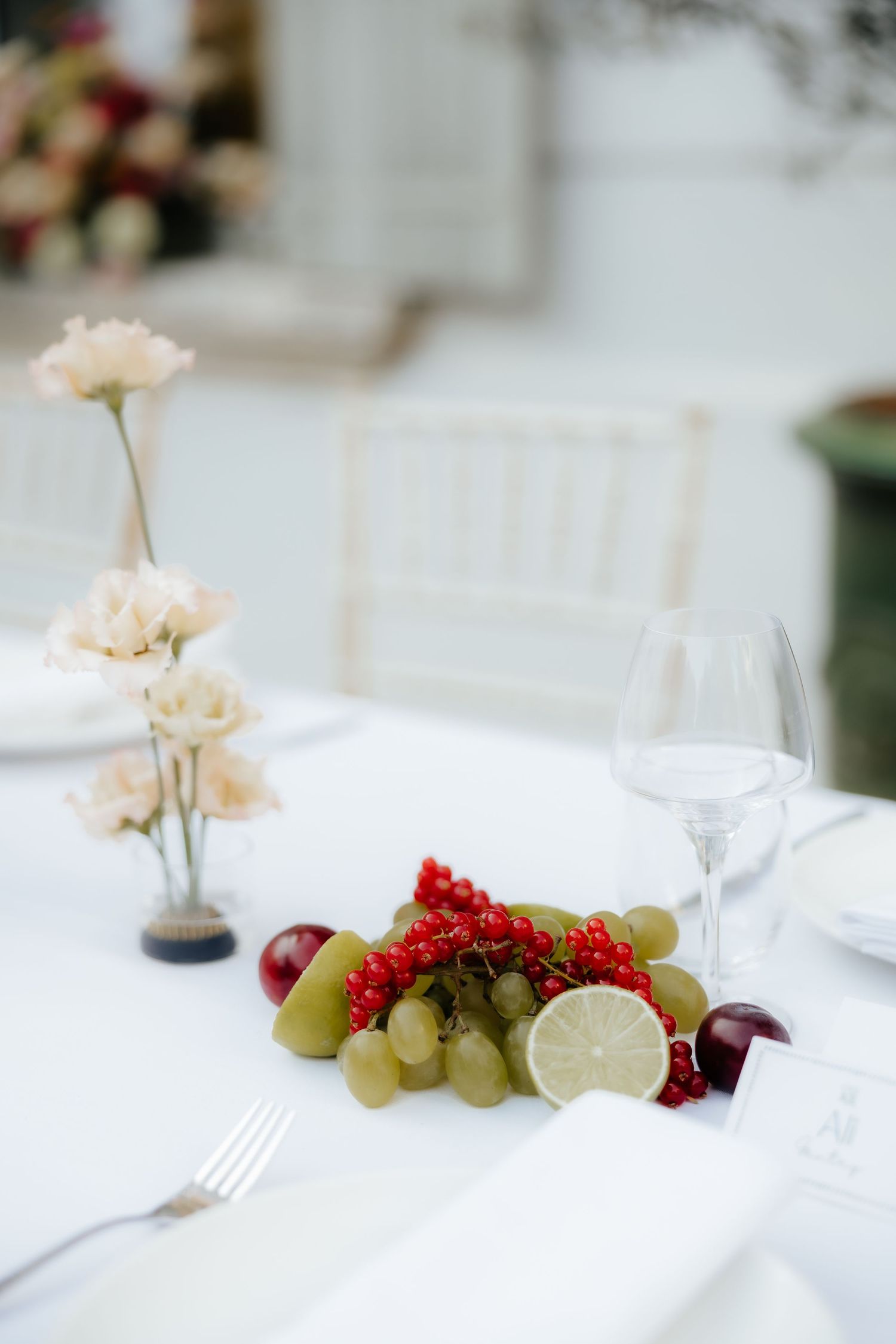 Elegant white table setting with fresh fruits, red berries, and delicate flowers creating a romantic dining atmosphere.