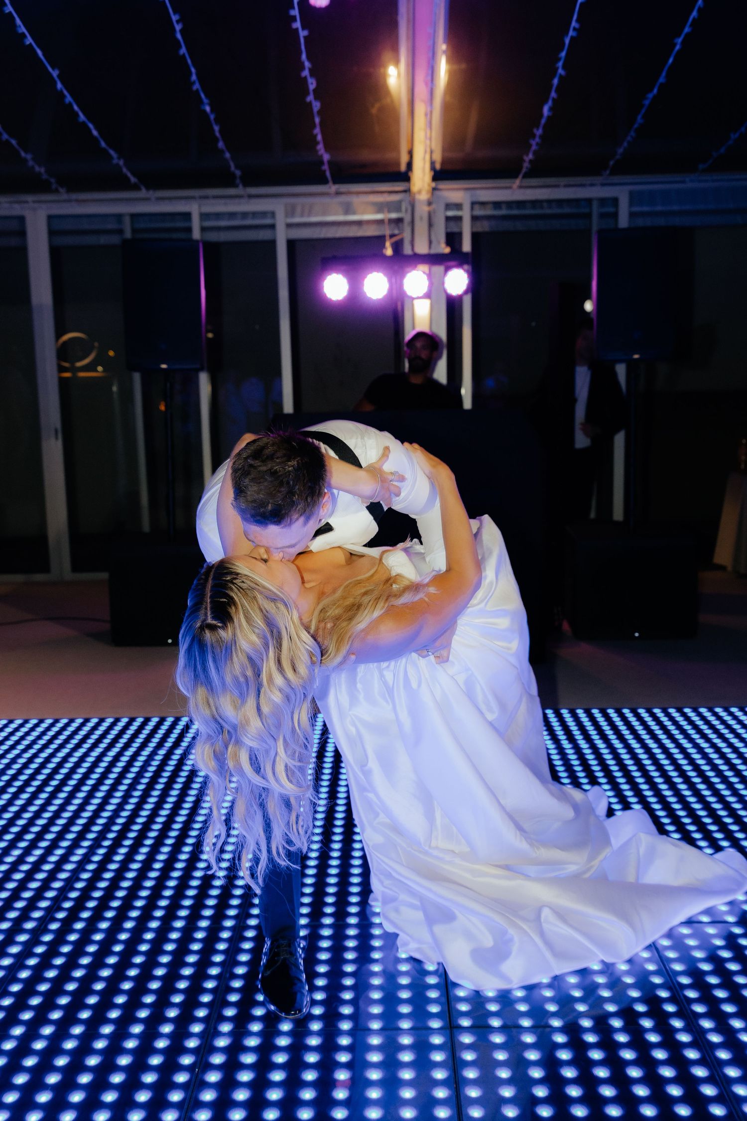 A dancer in flowing white fabric performs on an illuminated LED dance floor with blue and white checkerboard pattern.