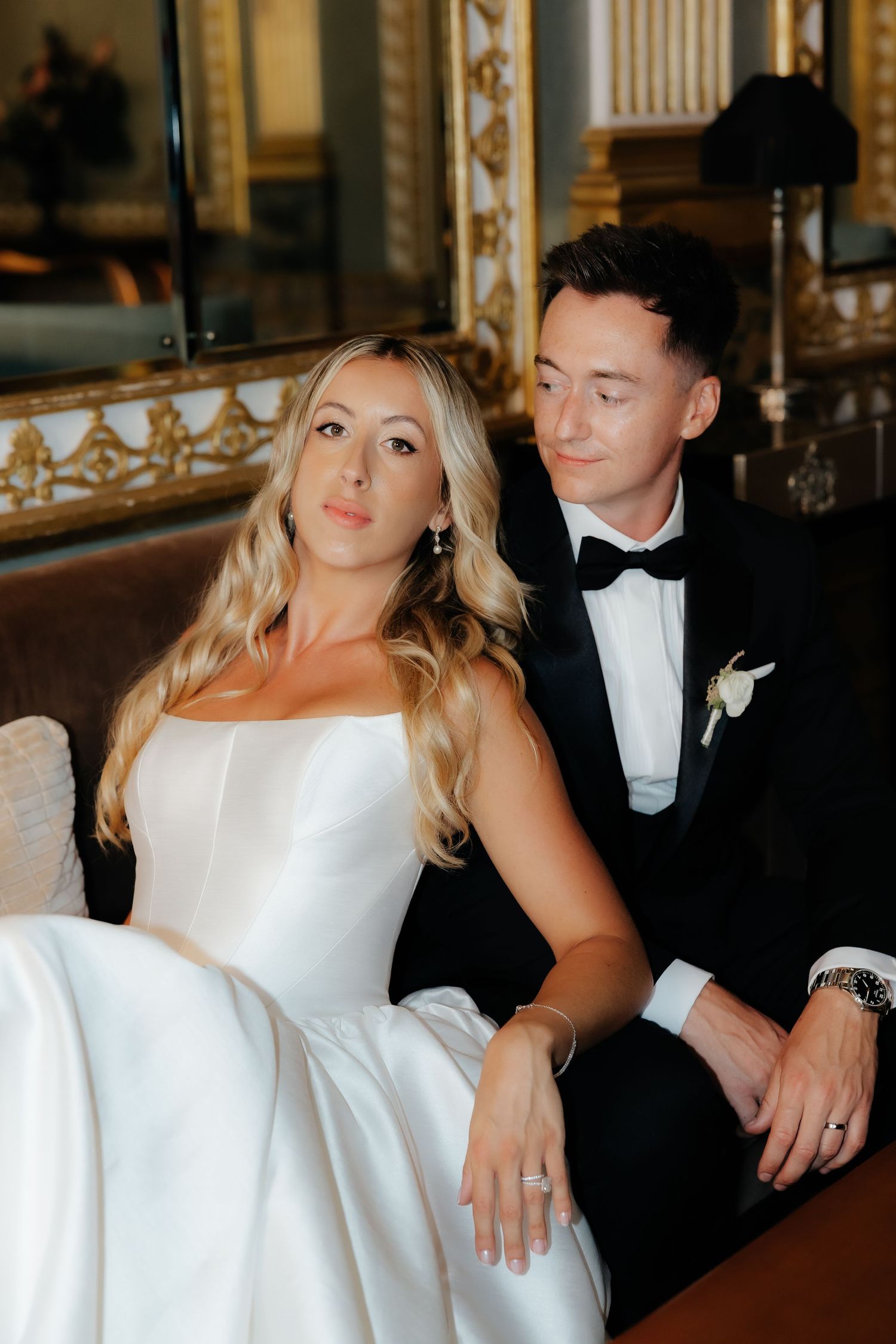 A bride and groom share intimate moments while sitting together in formal wedding attire.