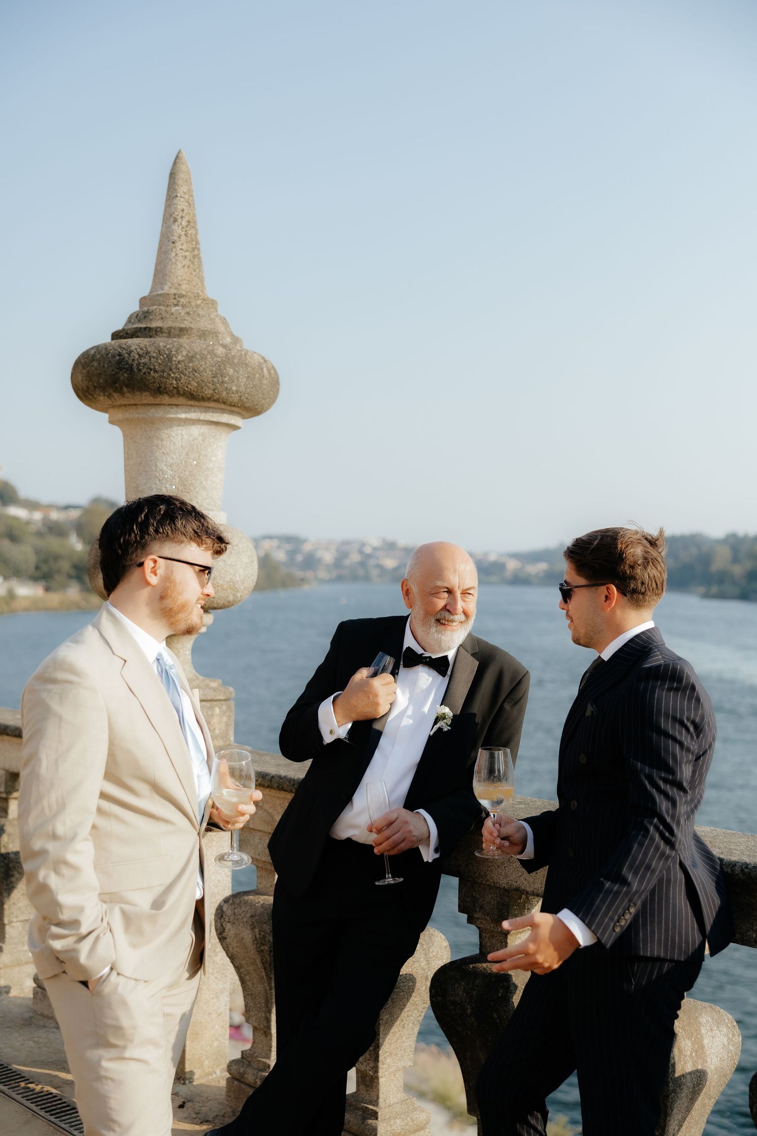 A group of people in formal attire share a candid moment of laughter by the waterfront.