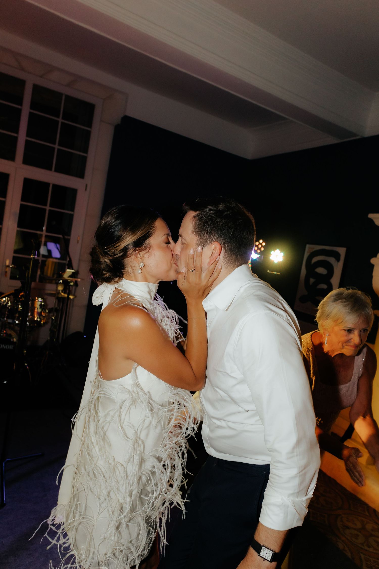 Wedding reception dance floor scene with guests dancing in an elegant venue with windows and ambient lighting.
