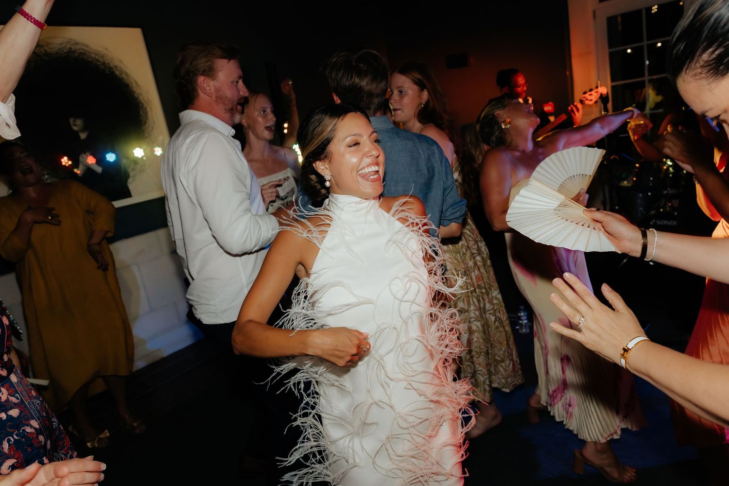 Wedding guests dancing and celebrating on a crowded dance floor during an evening reception.