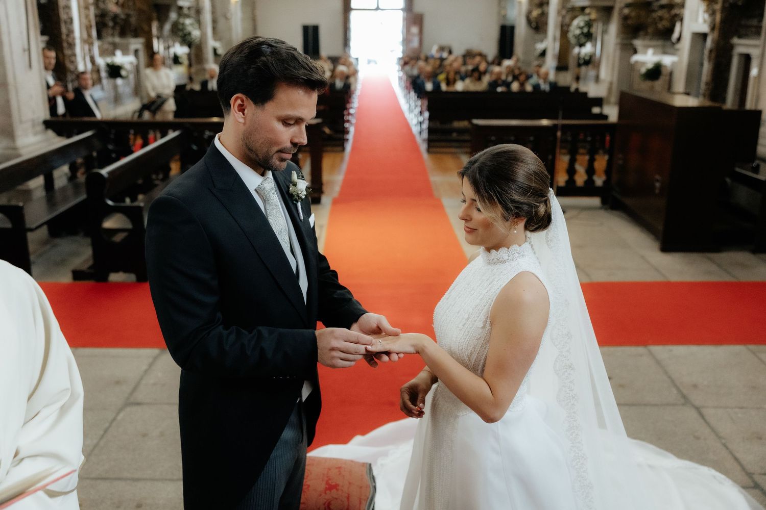 Groom places wedding ring on brides finger during church ceremony with red carpet aisle.