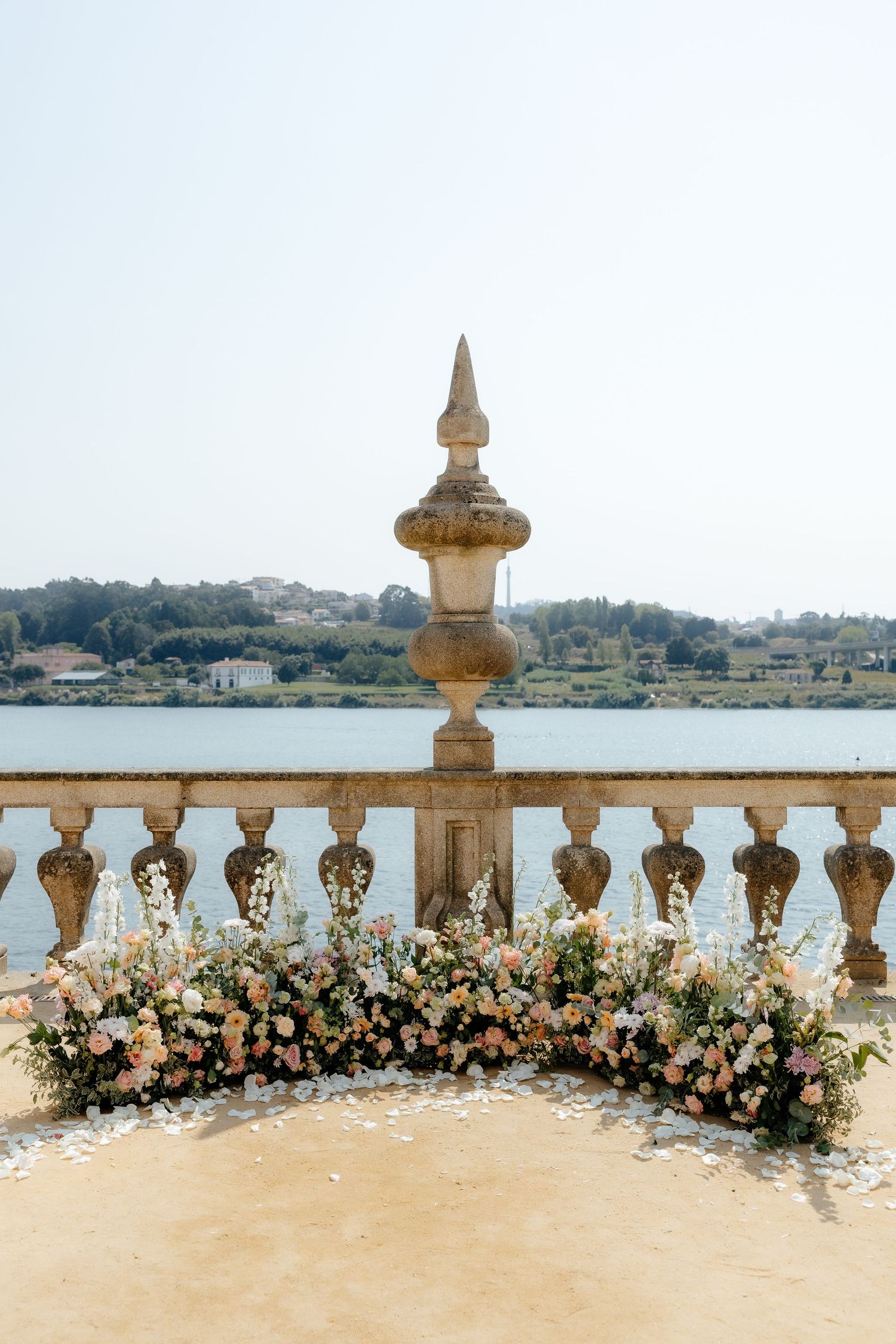 Stone balustrade terrace adorned with romantic pink and white floral arrangements overlooking a river.
