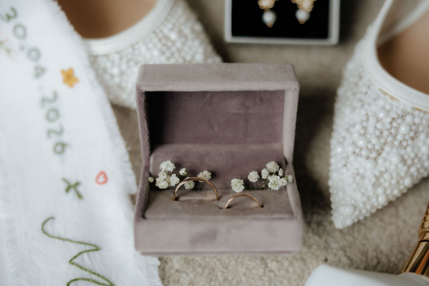 Close-up of wedding rings and floral hair accessories displayed in a velvet ring box.
