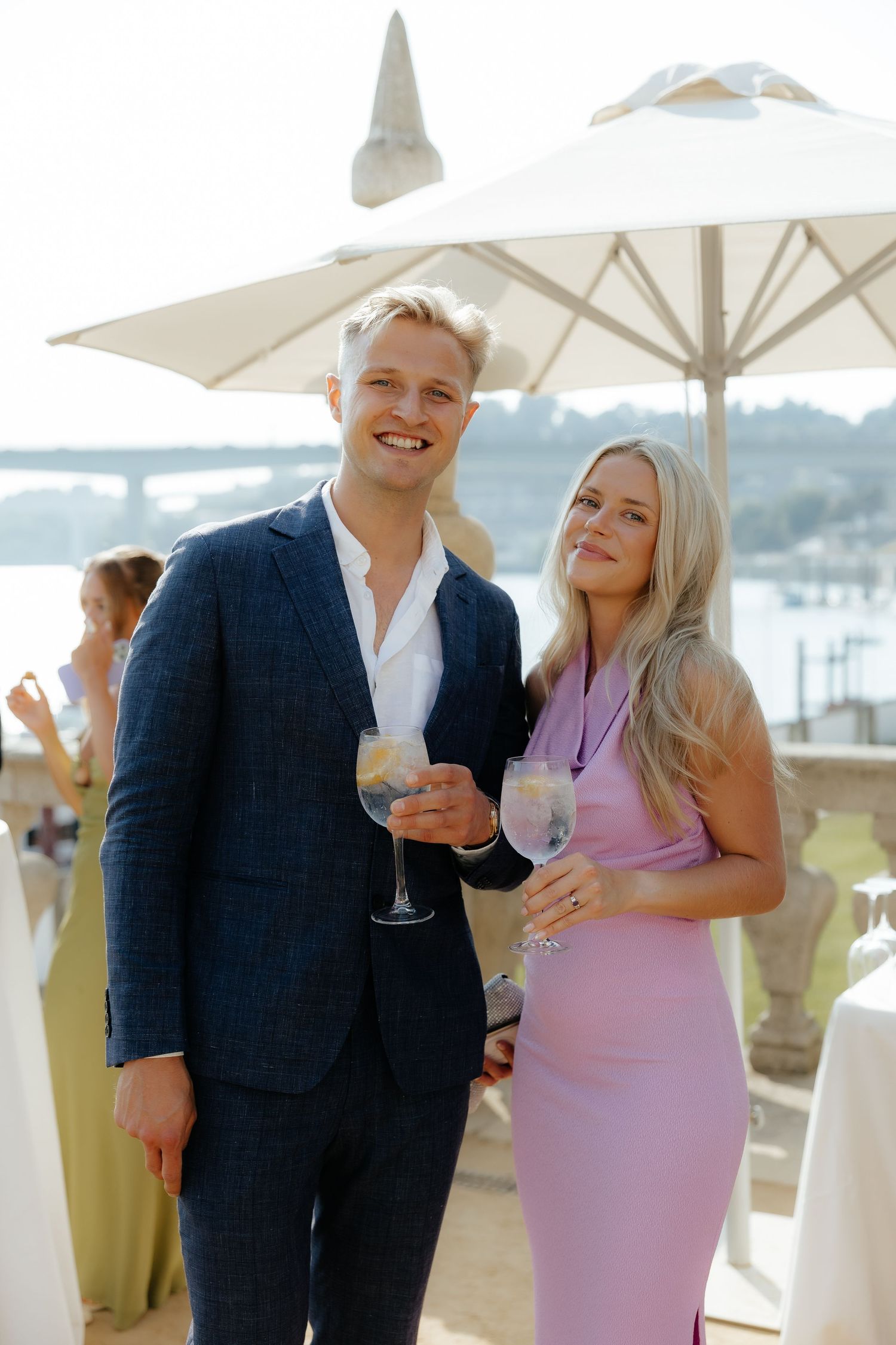 A couple in formal attire share a happy moment outdoors under white umbrellas at an elegant venue.
