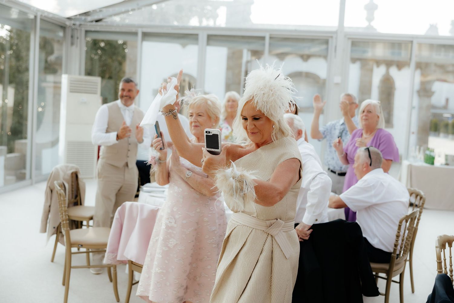 People dancing and celebrating at an elegant indoor event space with glass walls and natural lighting.