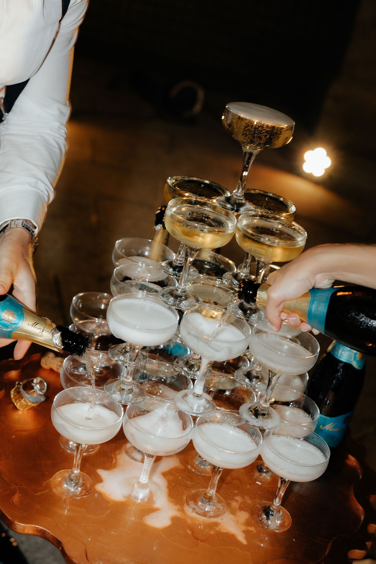 Champagne tower being poured at a celebration with coupe glasses stacked in elegant pyramid formation.