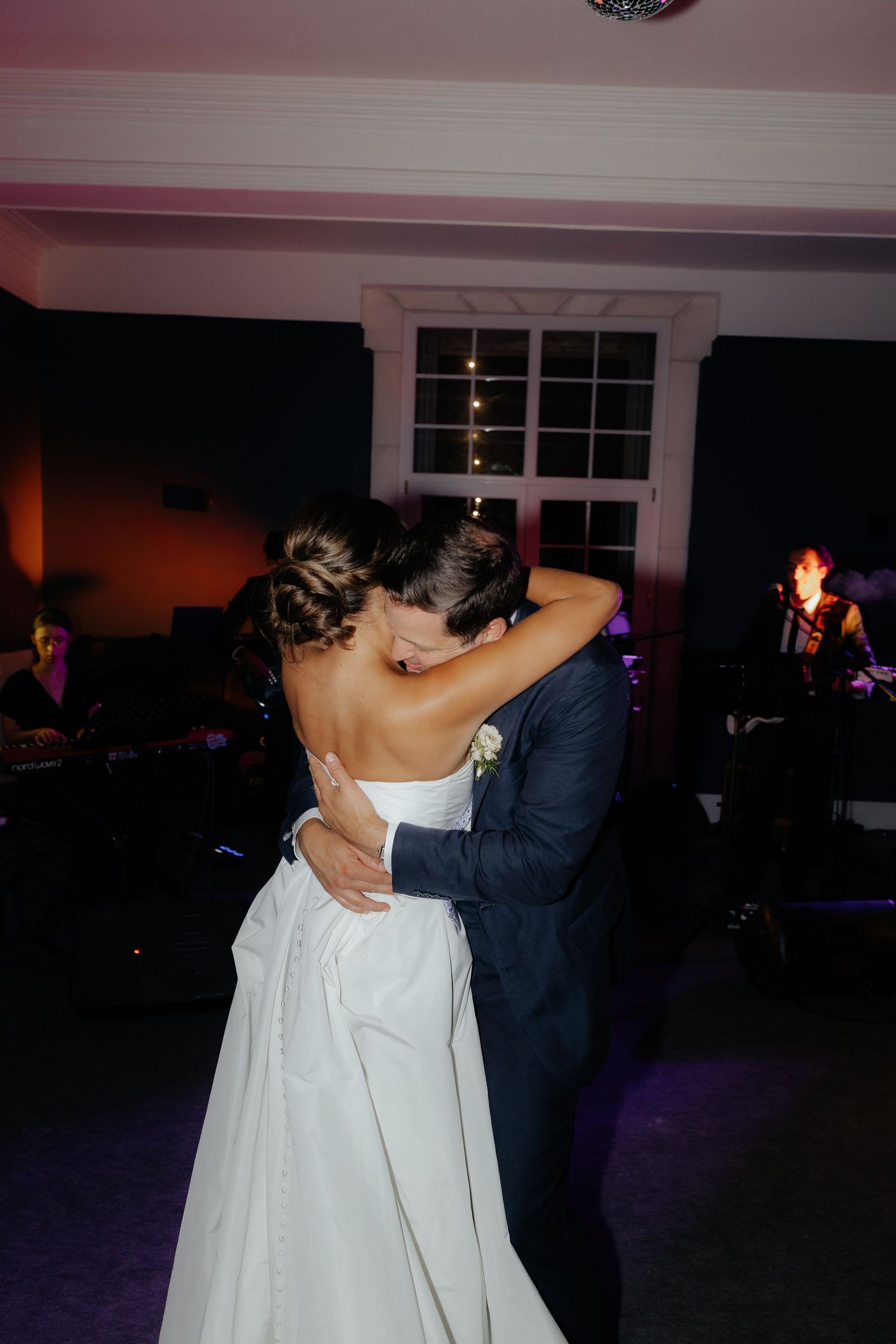A couple shares an intimate slow dance together at a dimly lit wedding reception.