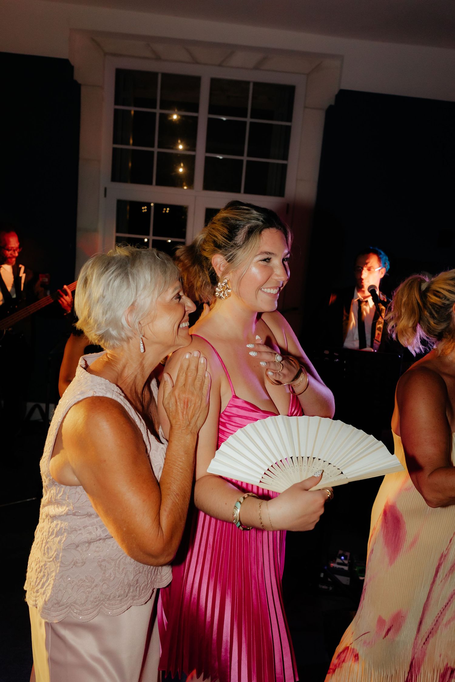 Wedding guests dance and fan themselves during a lively reception celebration at an indoor venue.