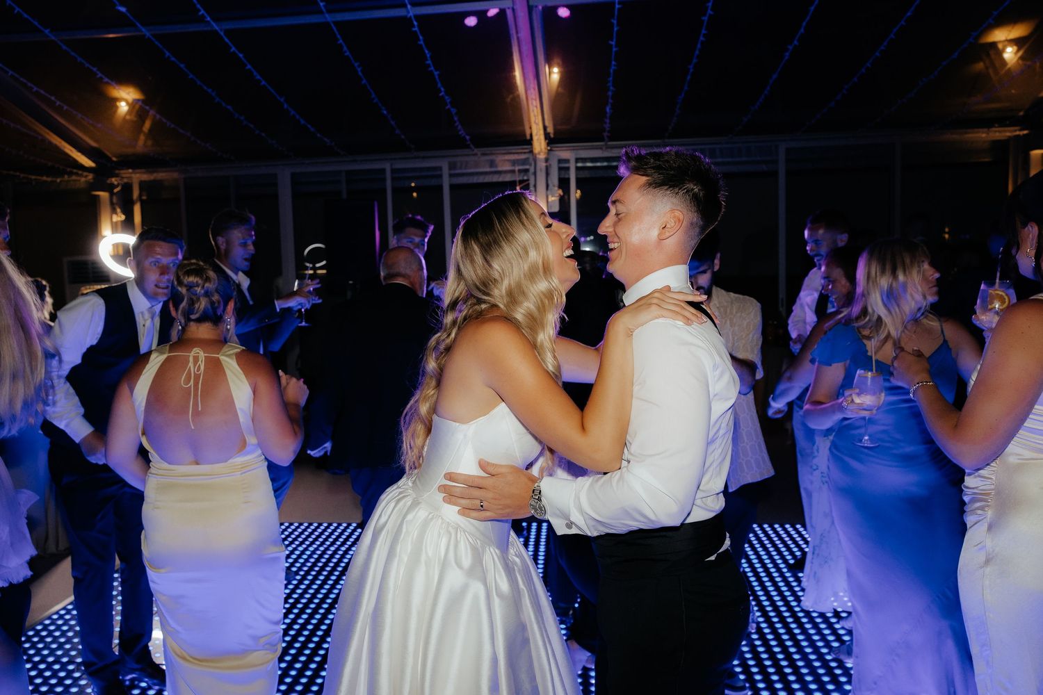 People dancing at a nightclub with blue and purple lighting on a checkered dance floor.