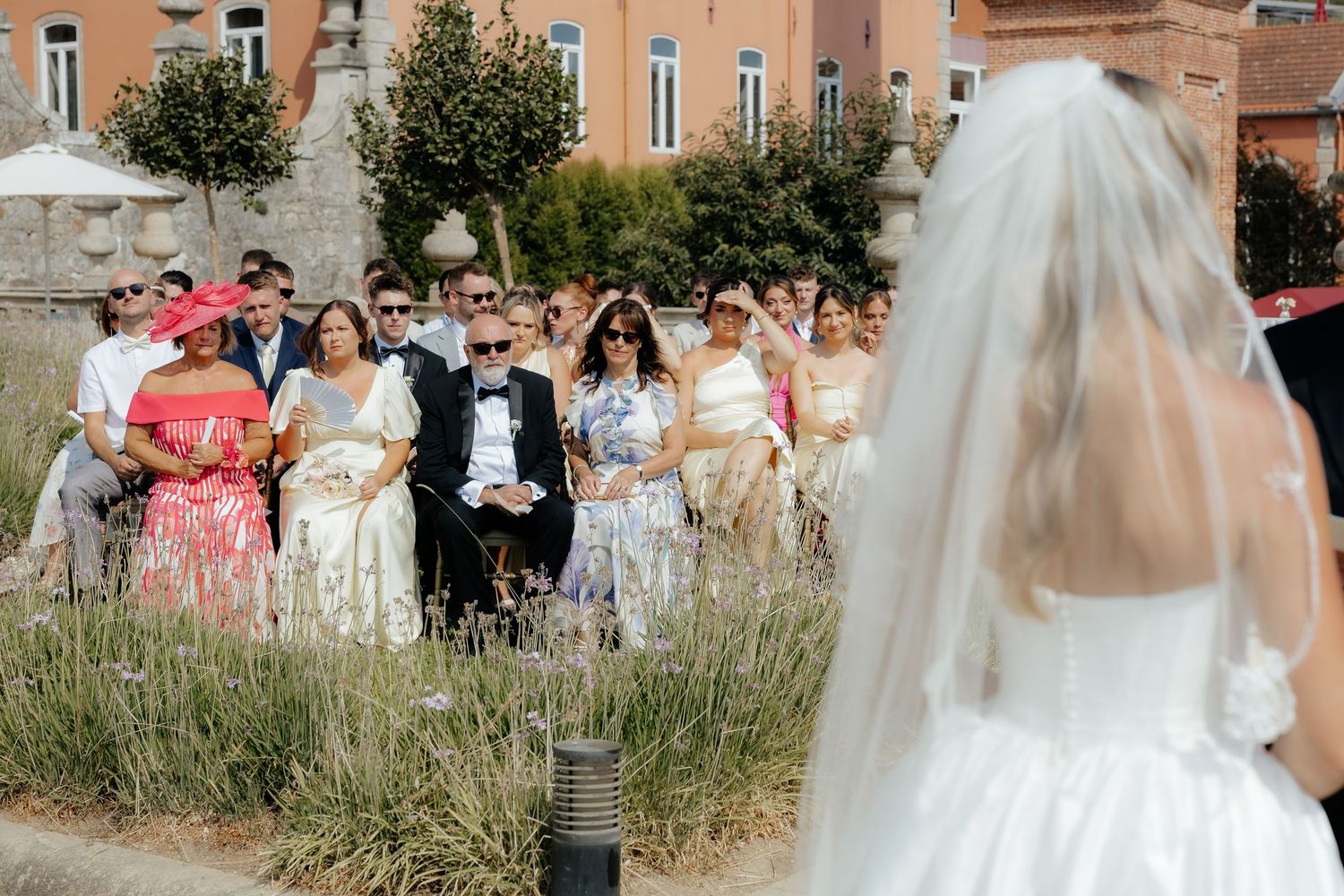 Wedding guests watch bride walk down aisle at outdoor ceremony surrounded by lavender garden.