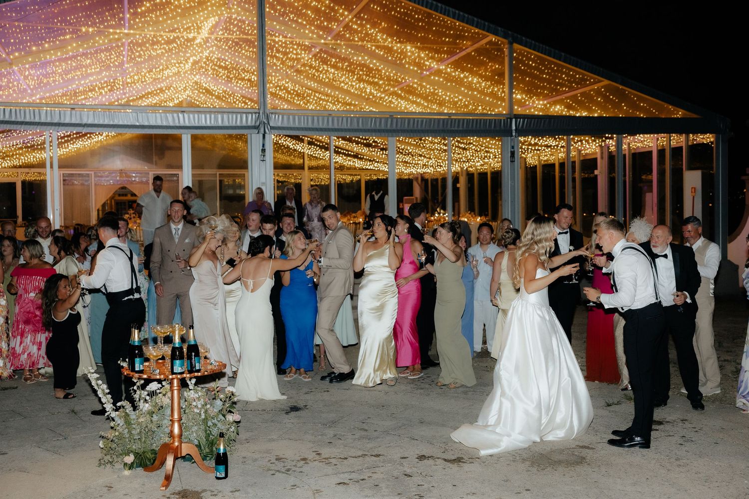 Wedding guests dance under a canopy of twinkling lights during an evening reception celebration.