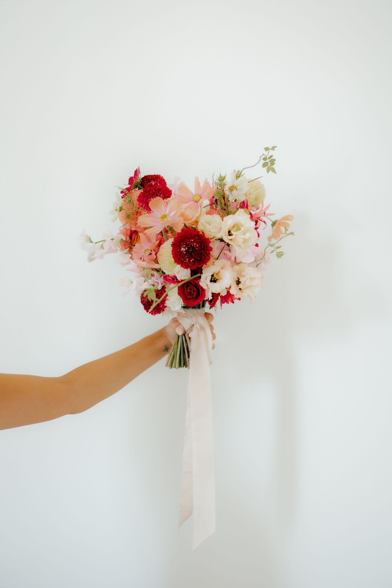 Delicate pink and red floral bouquet being held against a white background.