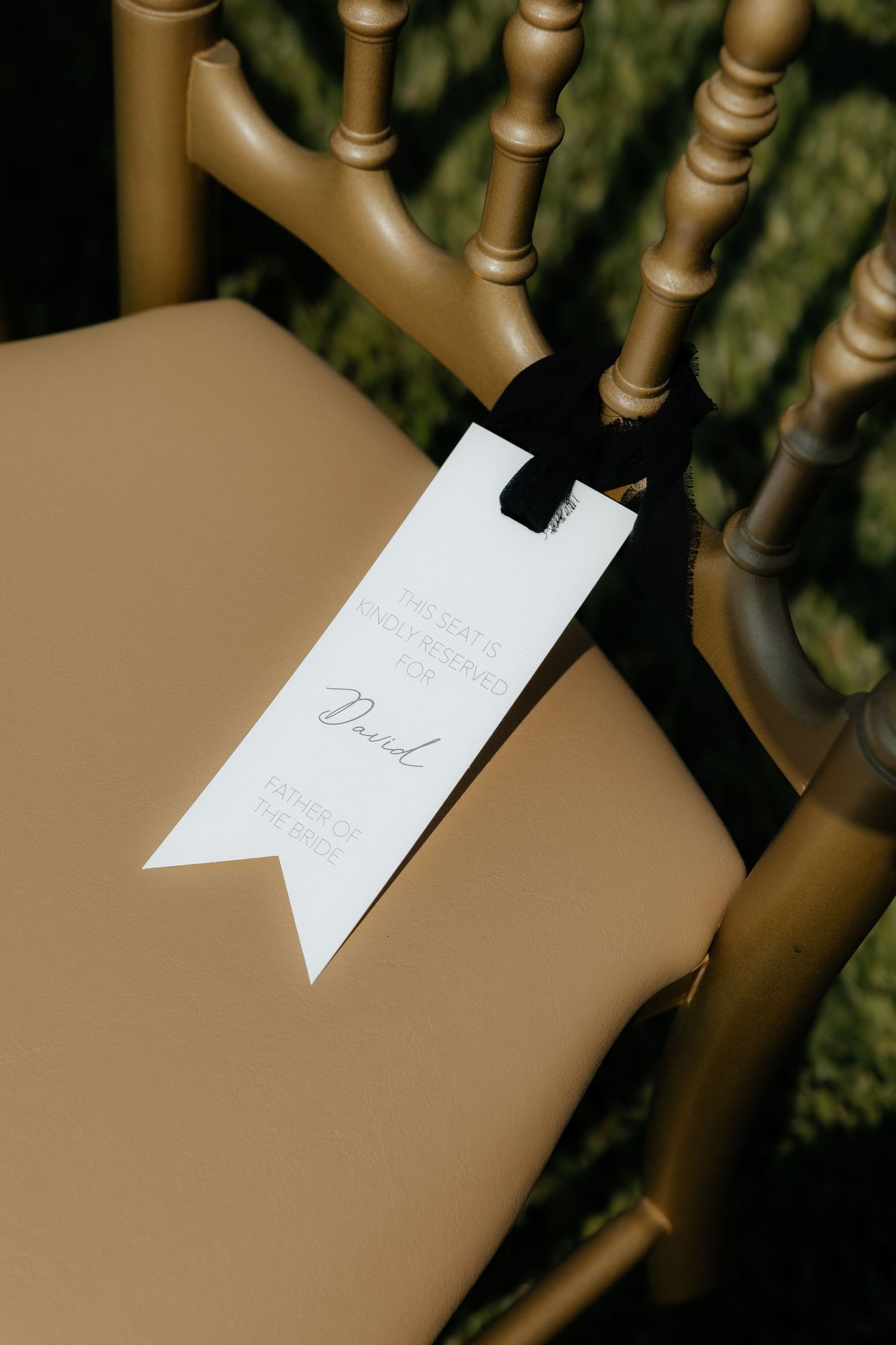 Elegant white wedding chair tag with black ribbon reading Father of the Bride on a gold chair.