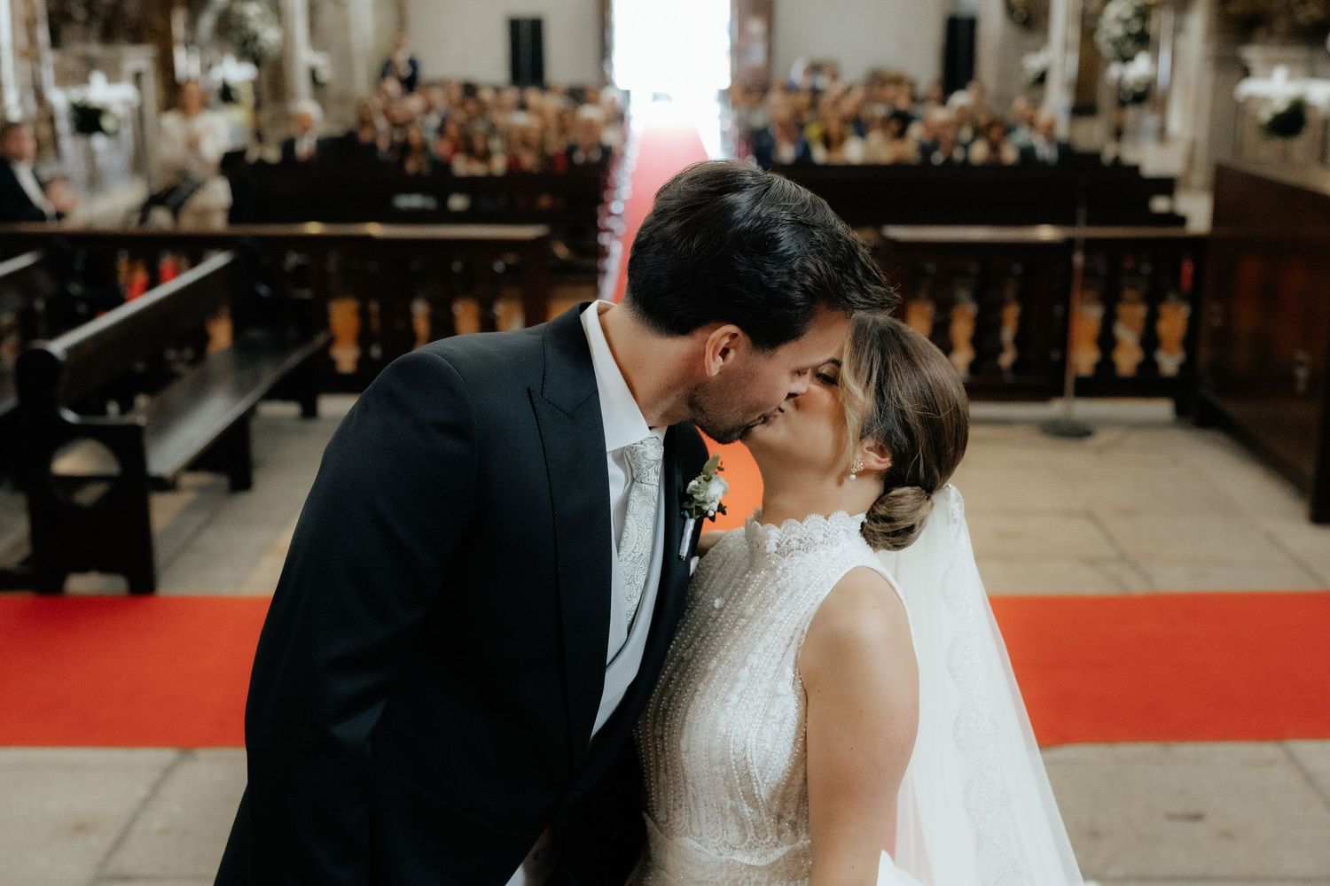 Bride and groom share a romantic first kiss at the altar of an ornate church.