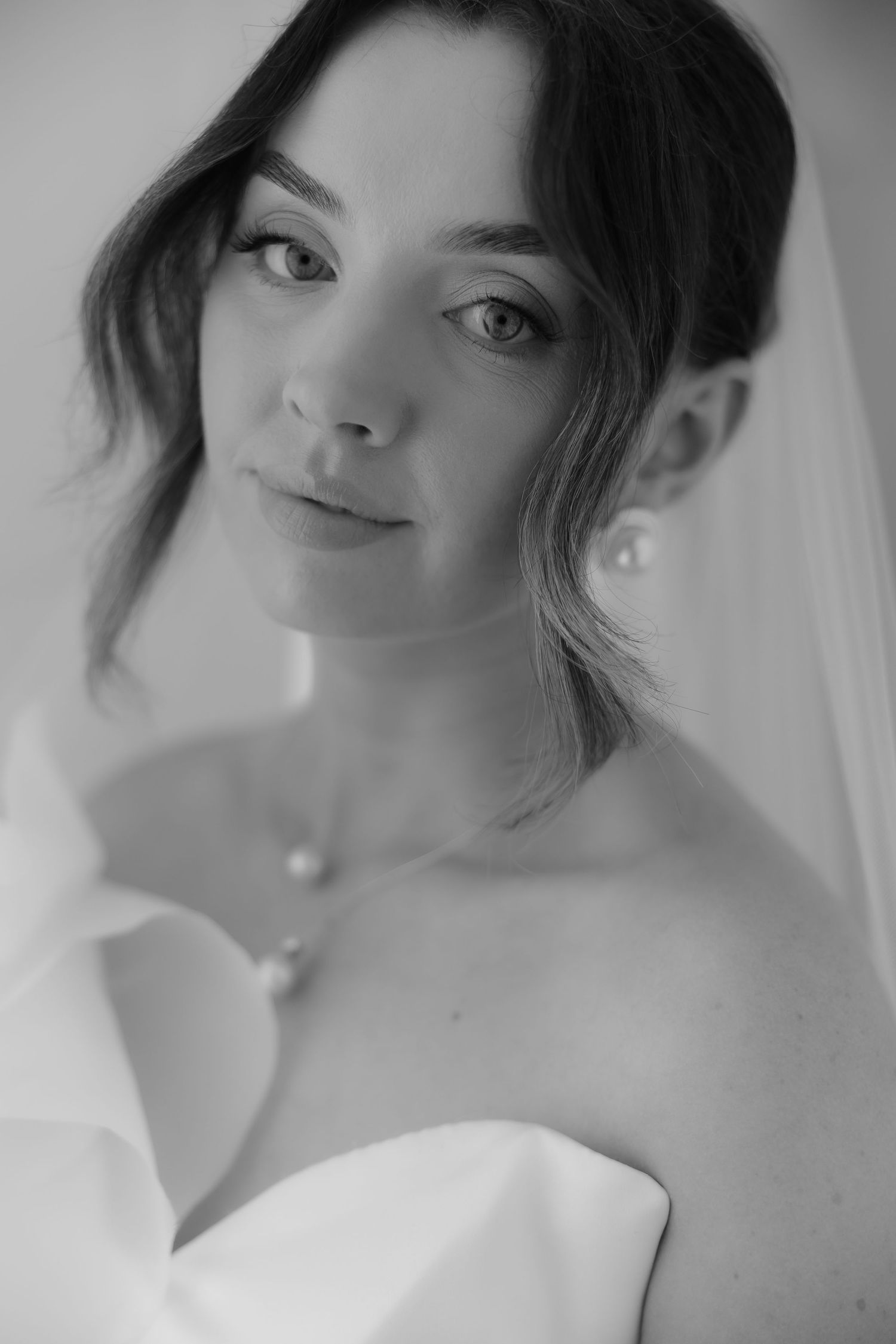 Black and white bridal portrait of a young woman in a strapless gown wearing pearl earrings and necklace.