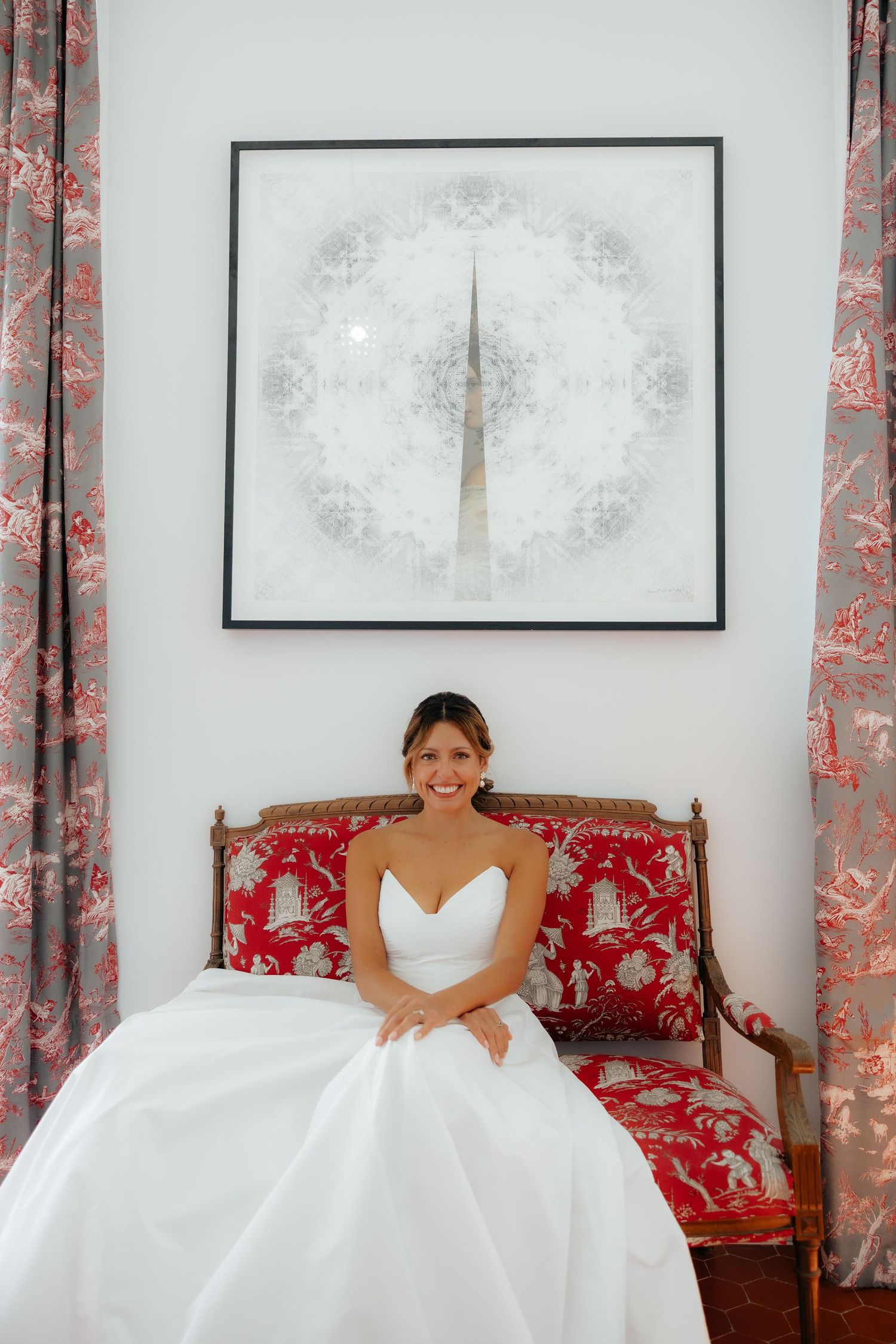 Elegant white wedding dress displayed in a room with red floral curtains and antique furniture.
