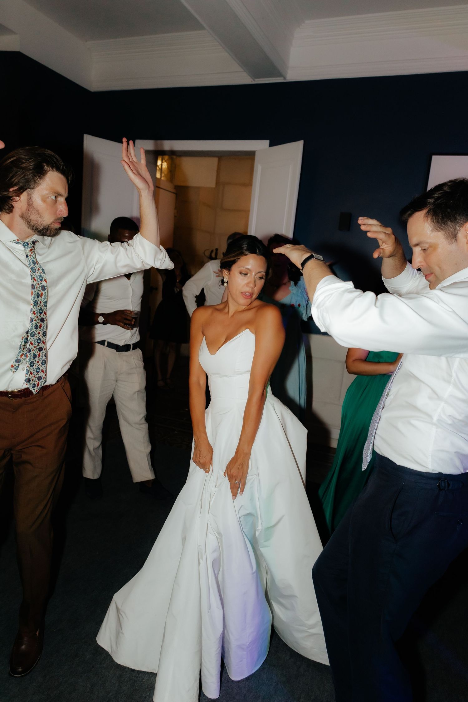Wedding guests dancing together at a reception, with people in white formal attire moving energetically on the dance floor.