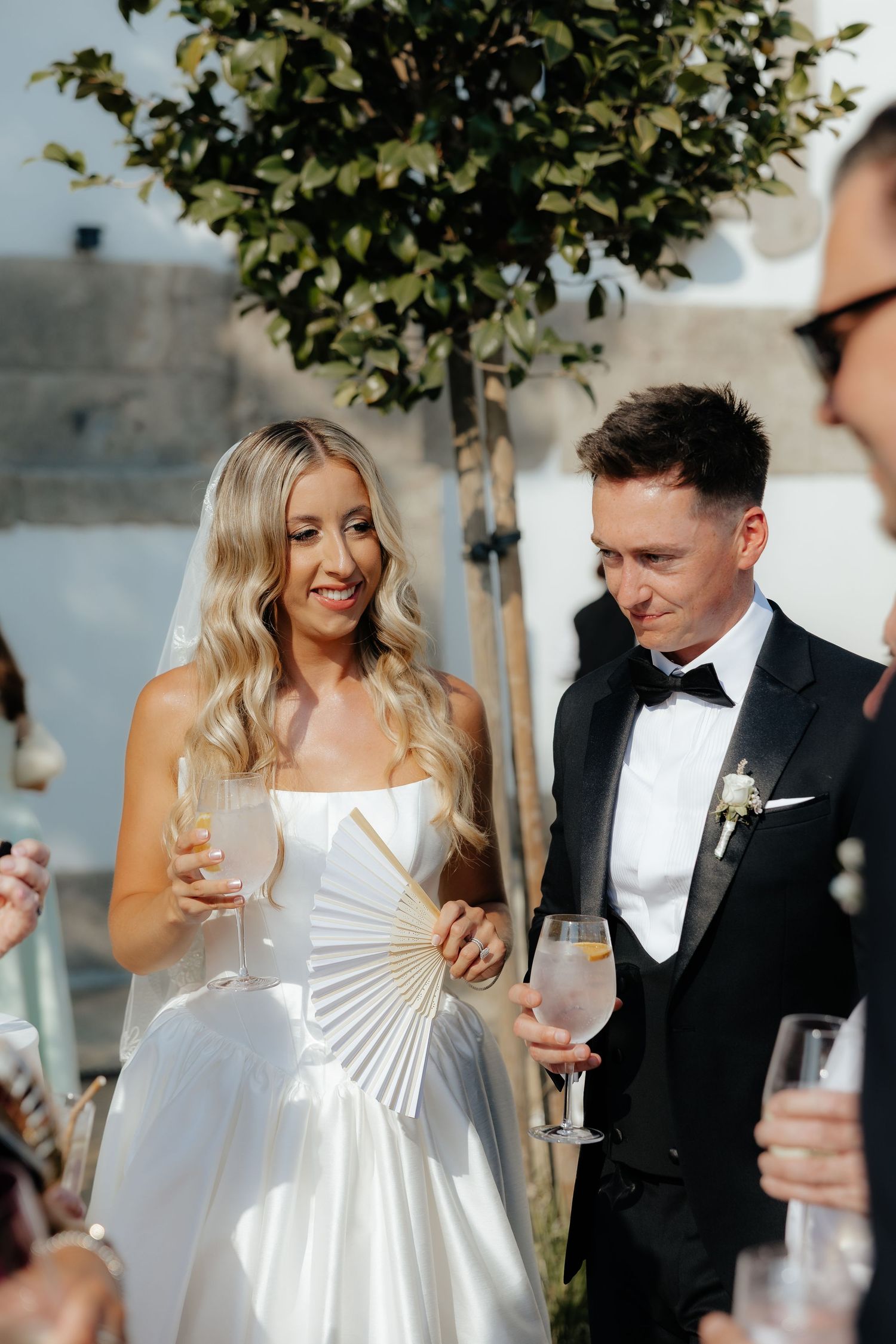 A bride and groom share joyful candid moments together under trees at their elegant outdoor wedding celebration.