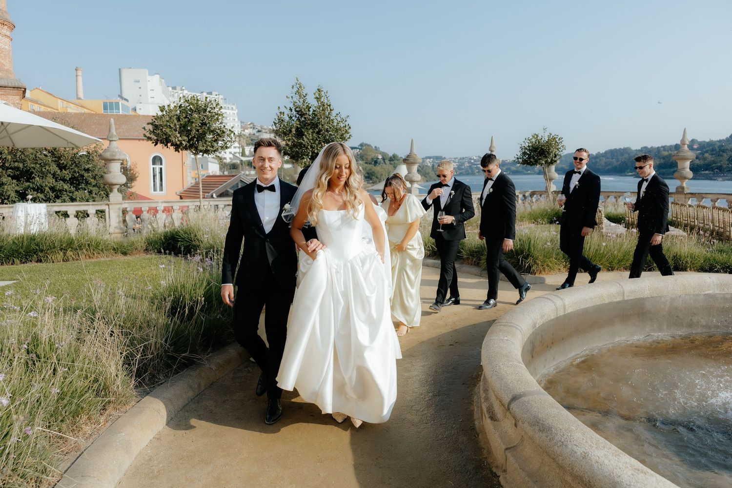 Wedding party walks along a curved coastal path with ocean views on a sunny afternoon.