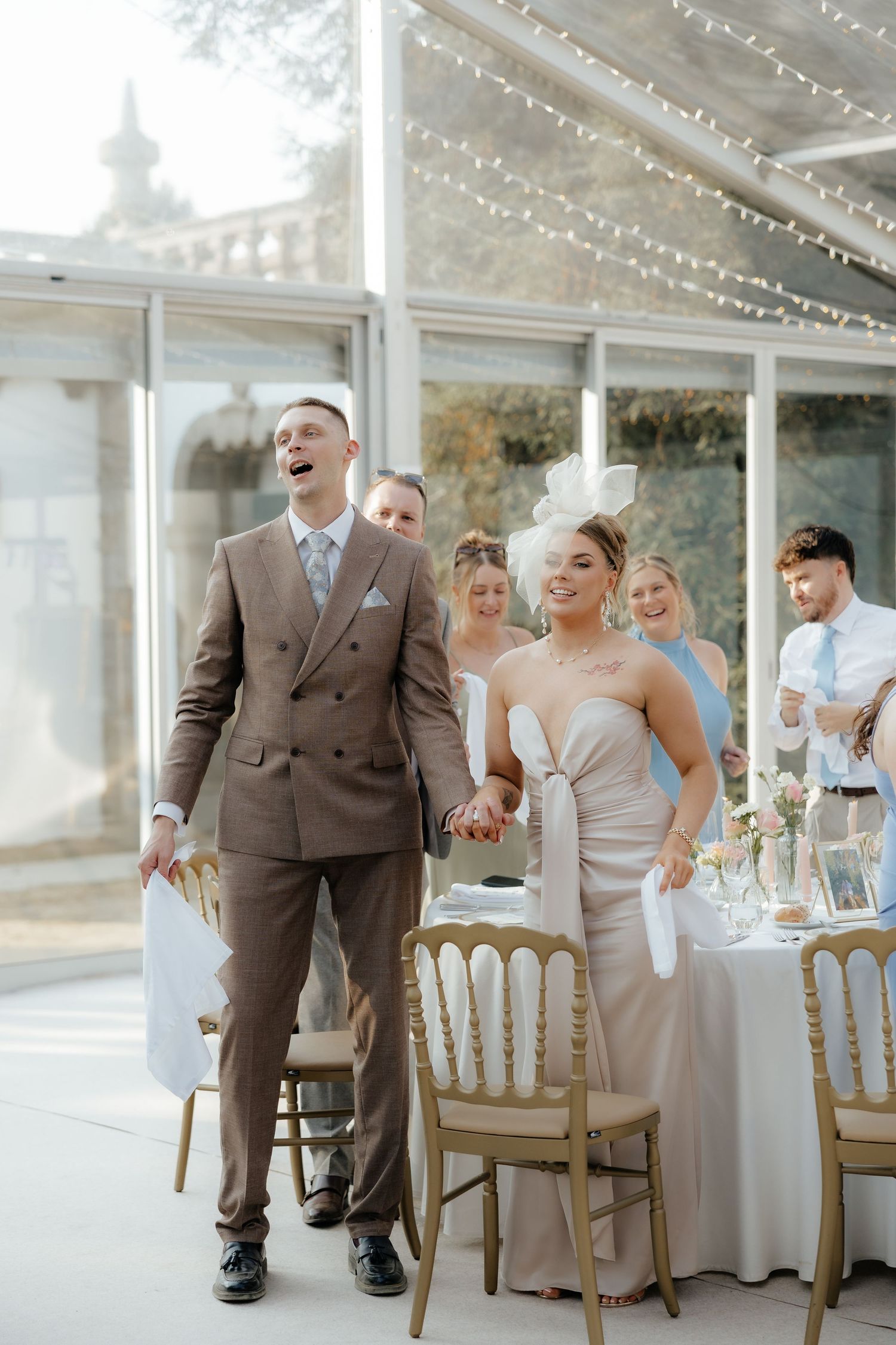 Wedding guests sharing joyful laughter at an elegant reception under a glass ceiling conservatory.