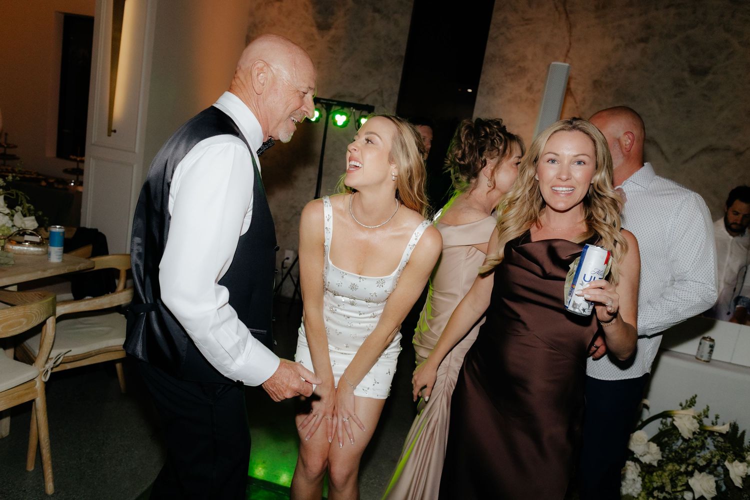 Wedding guests socializing and dancing together in elegant venue with green stage lighting at reception.