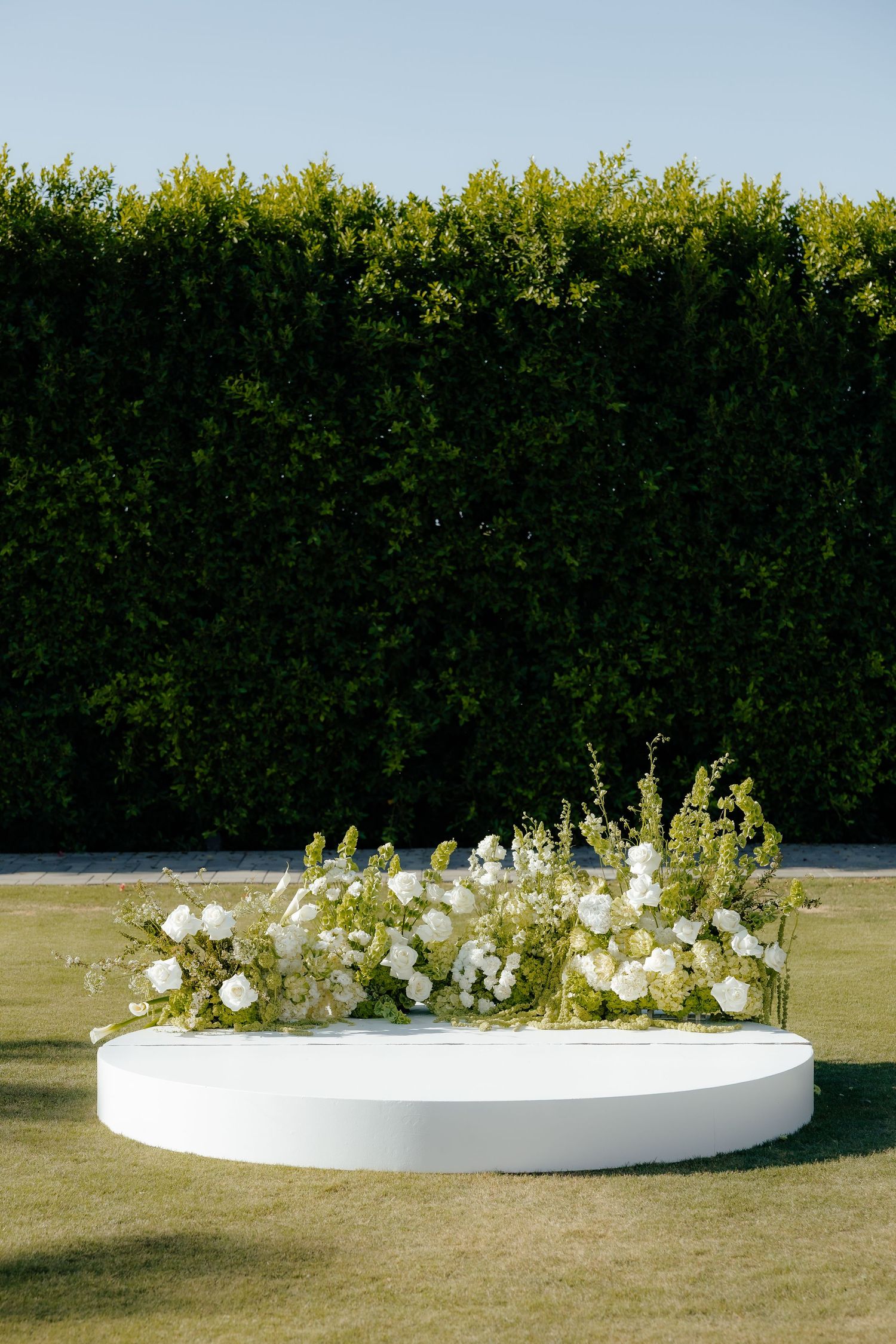 Elegant circular white wedding altar adorned with white floral arrangements on green grass.