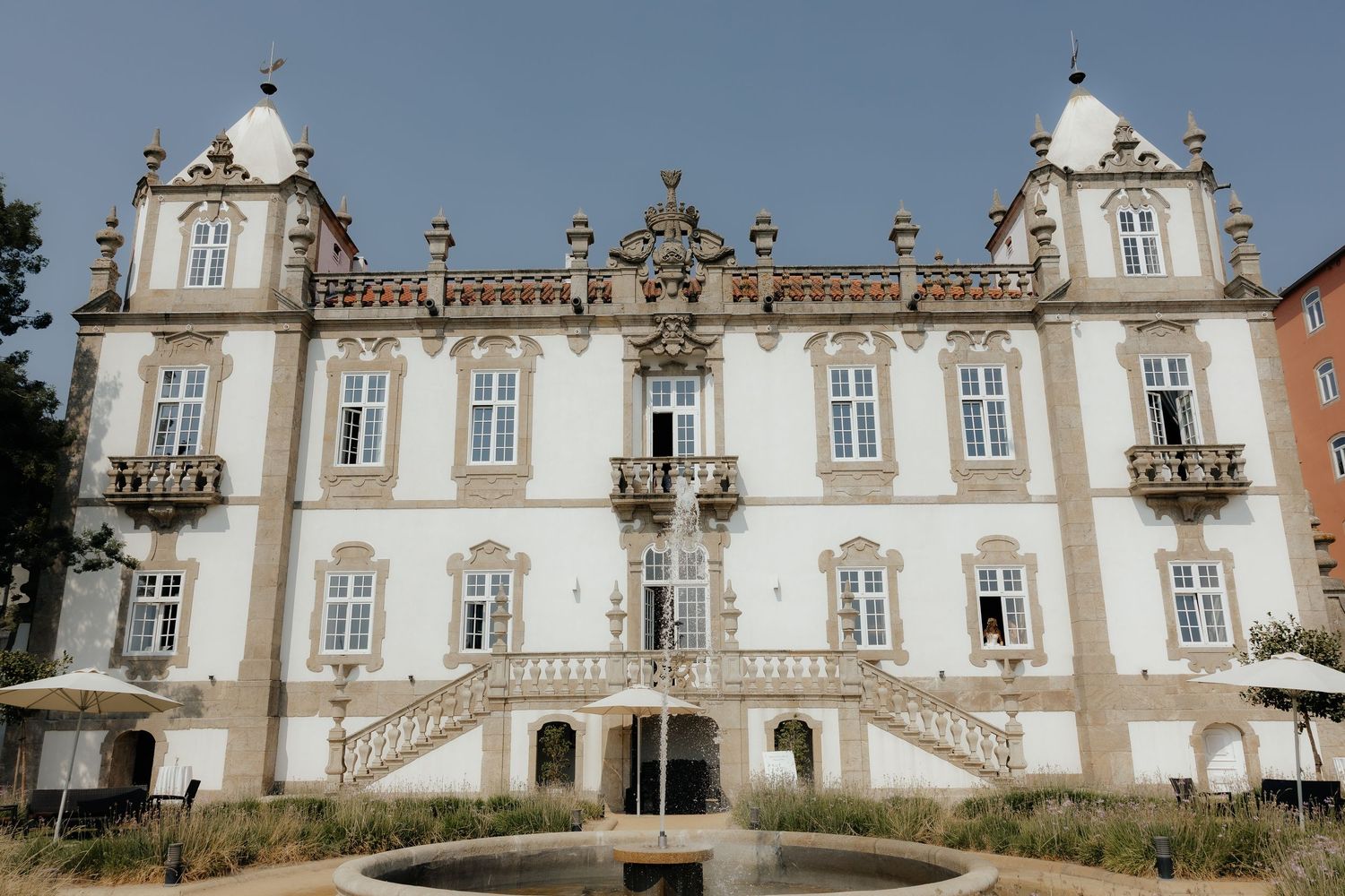 Grand white Baroque palace facade with ornate balconies, decorative spires, and a central fountain.