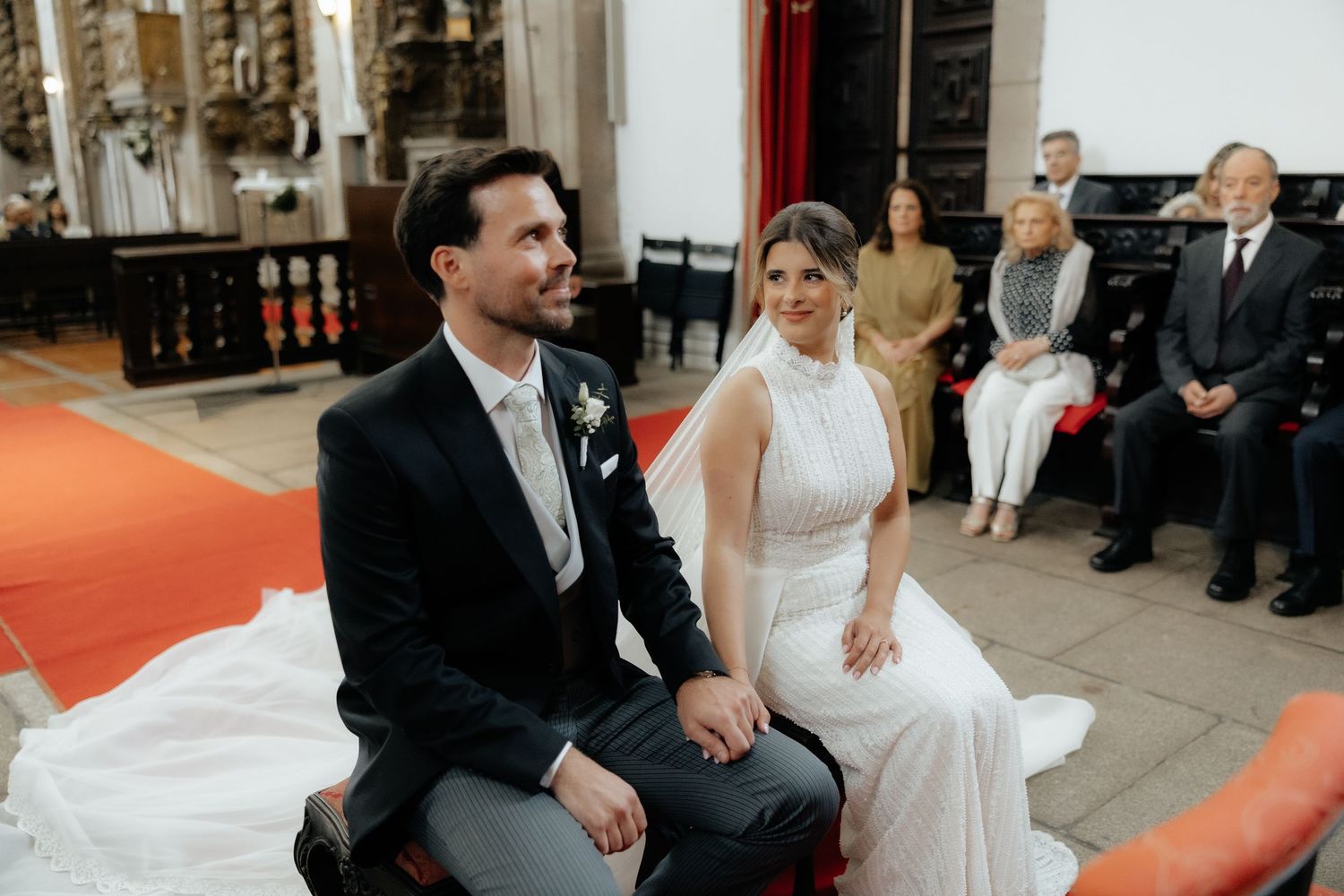Bride and groom sit together smiling during wedding ceremony in ornate church.
