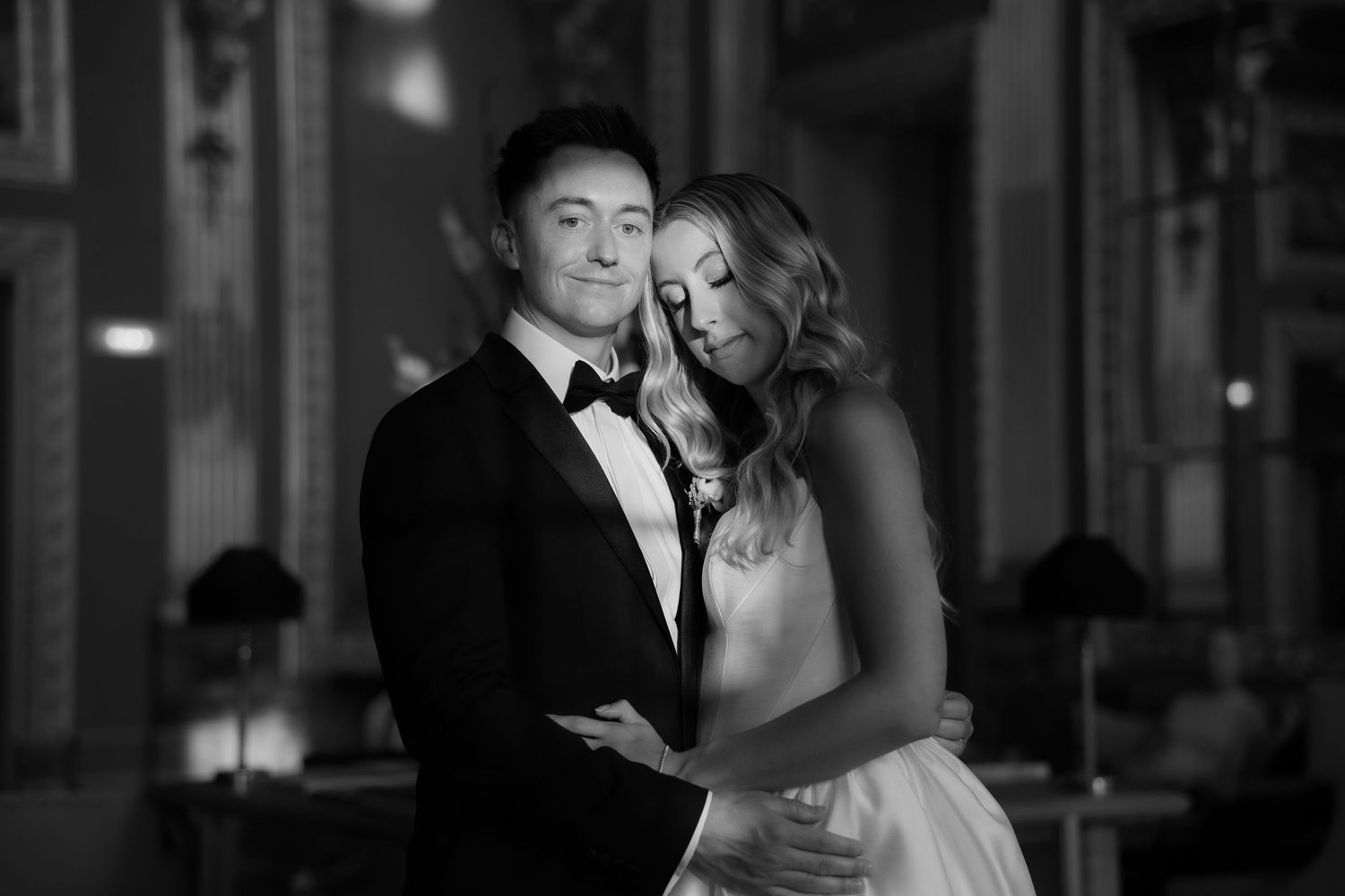 Elegant black and white portrait of bride and groom embracing in a beautifully decorated wedding venue.