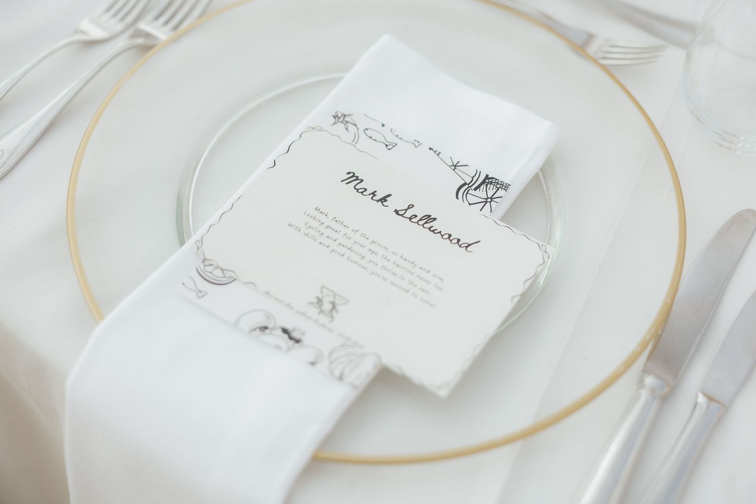 Elegant white and gold place settings with delicate calligraphy name cards on glass charger plates.