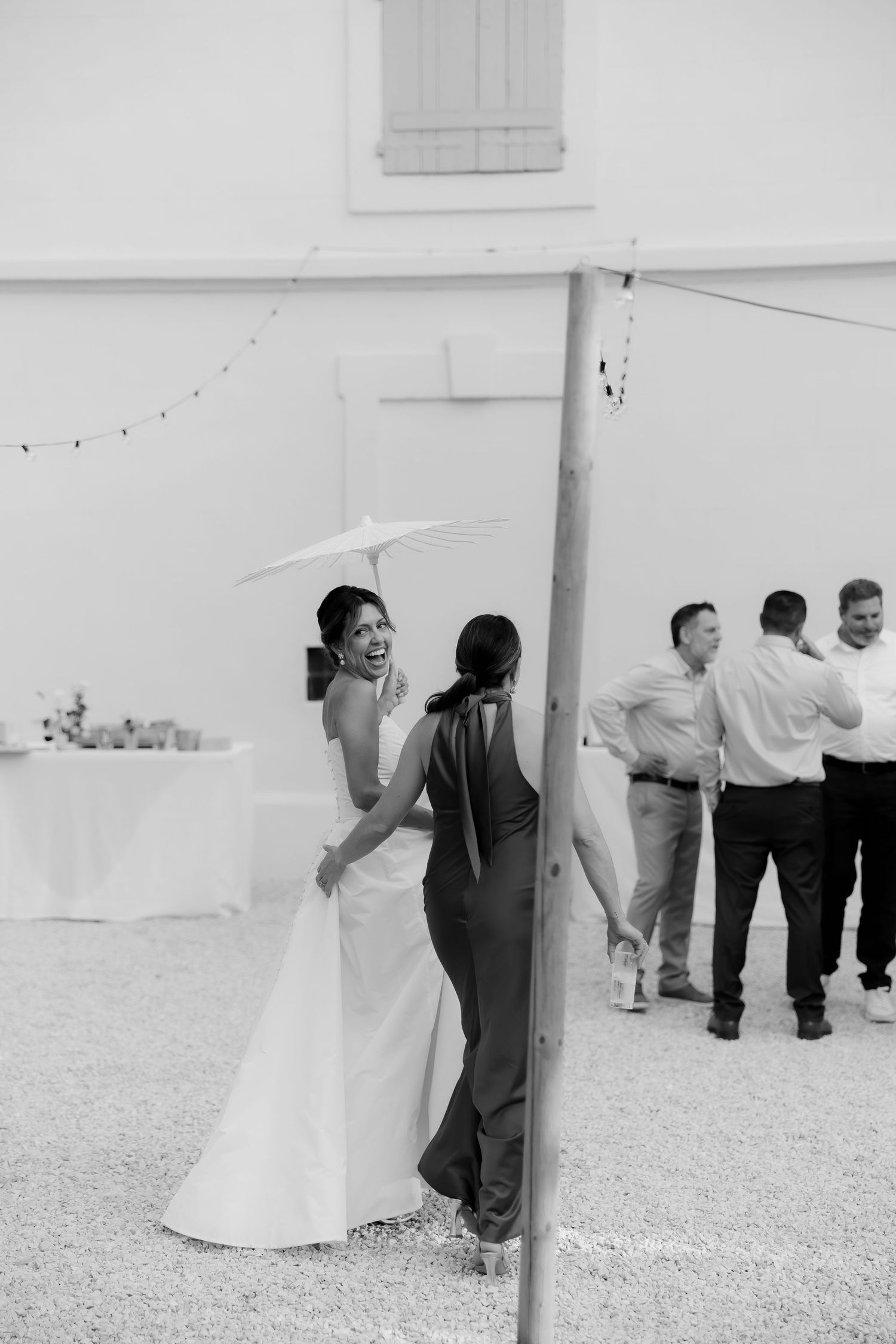 A black and white candid moment at a wedding reception with guests mingling outdoors.