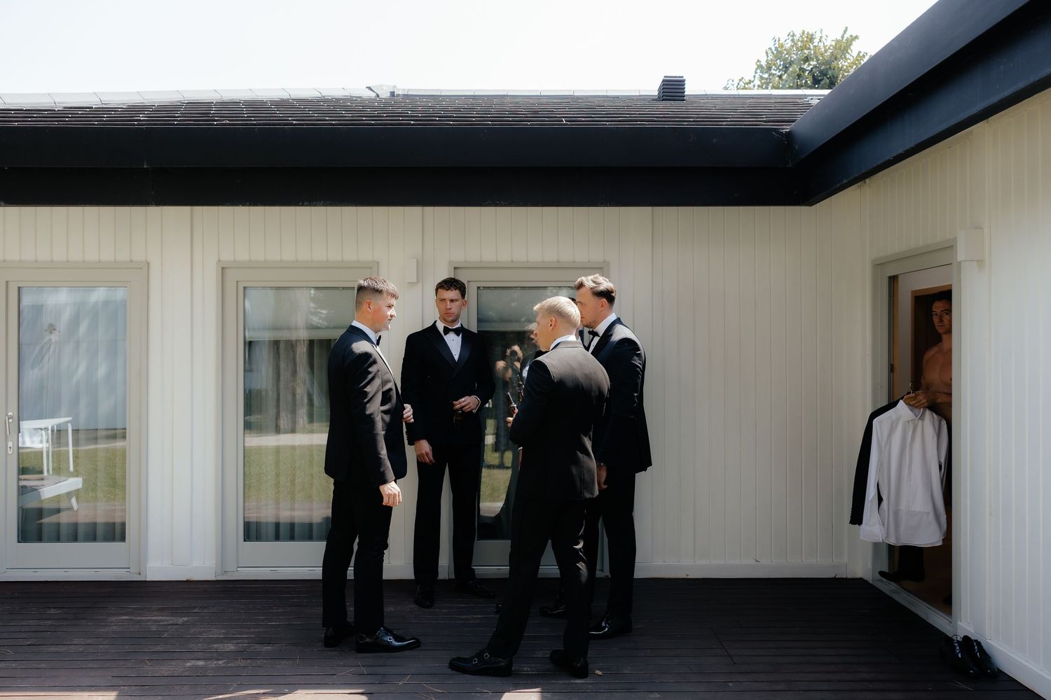 A group of people in formal attire gather in conversation outside a modern white building with dark trim details.