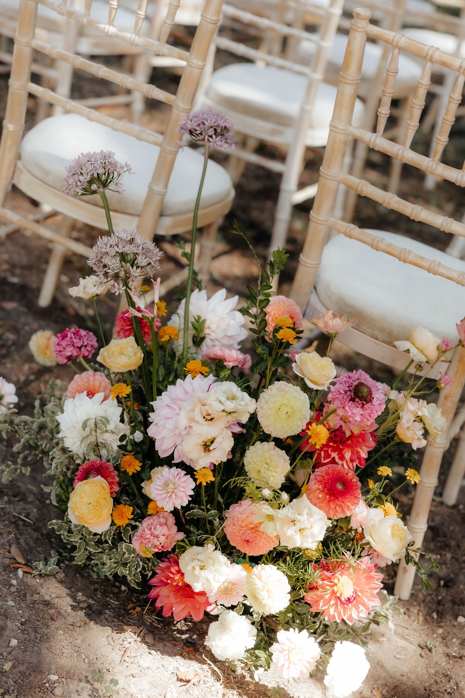 Colorful floral arrangements with pink, peach and white blooms line wedding ceremony aisle.