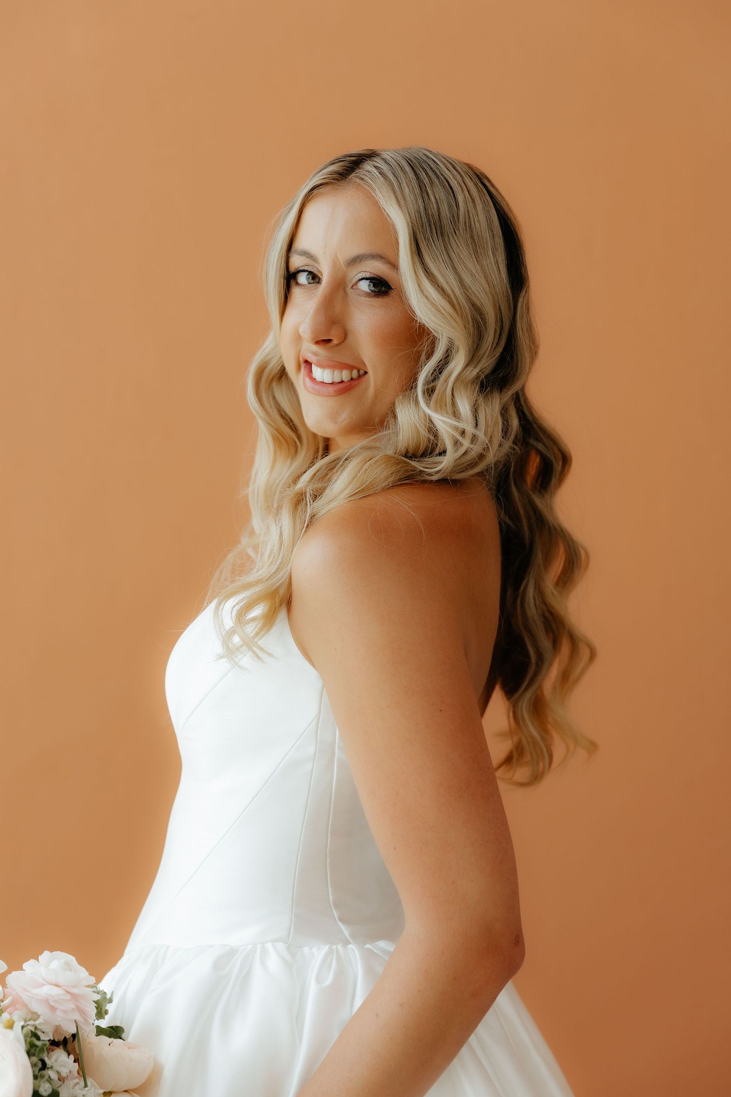 A bride in a white wedding dress poses against a warm terracotta background in a series of candid shots.