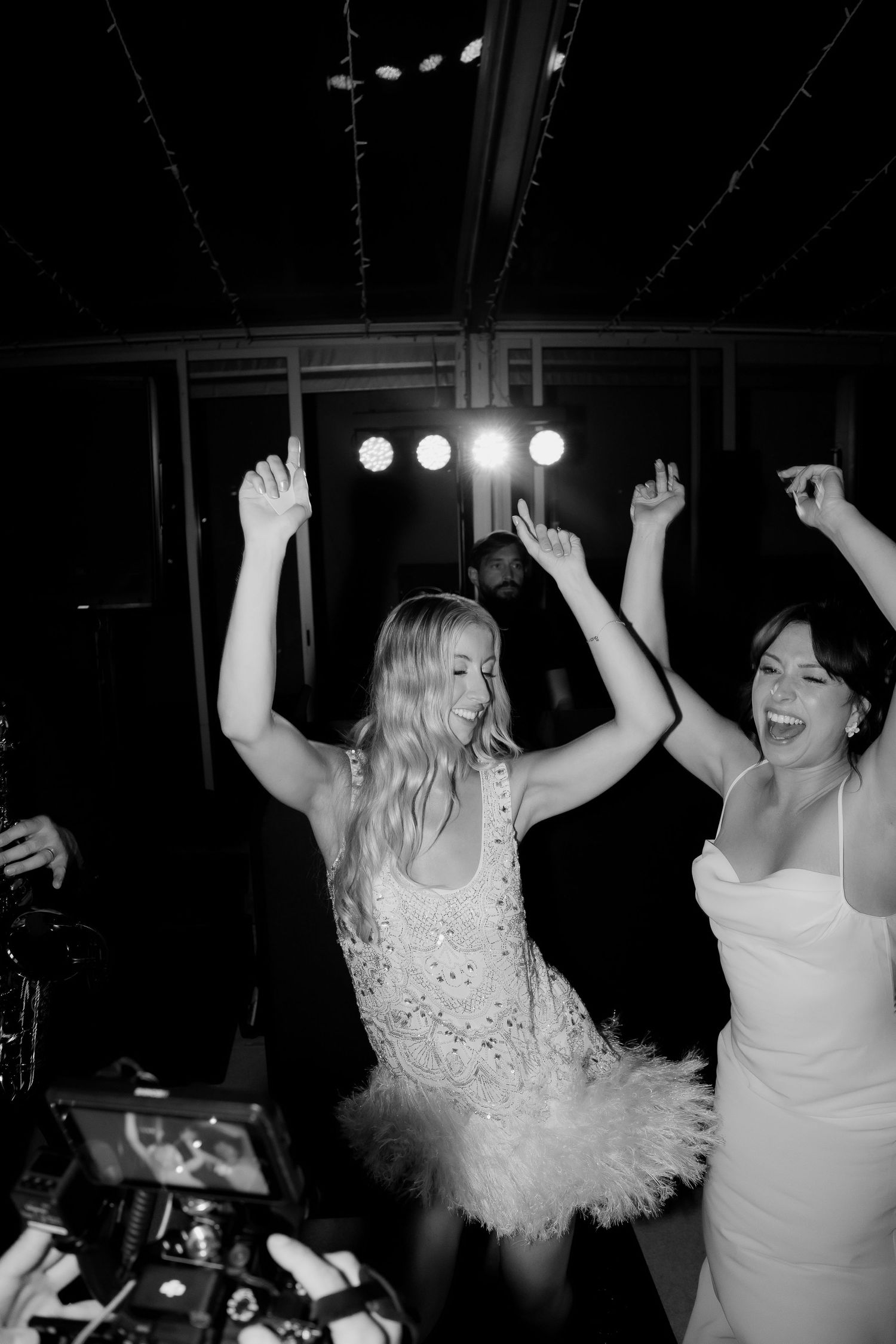 A group of people dancing and celebrating at a nighttime party with stage lighting in the background.