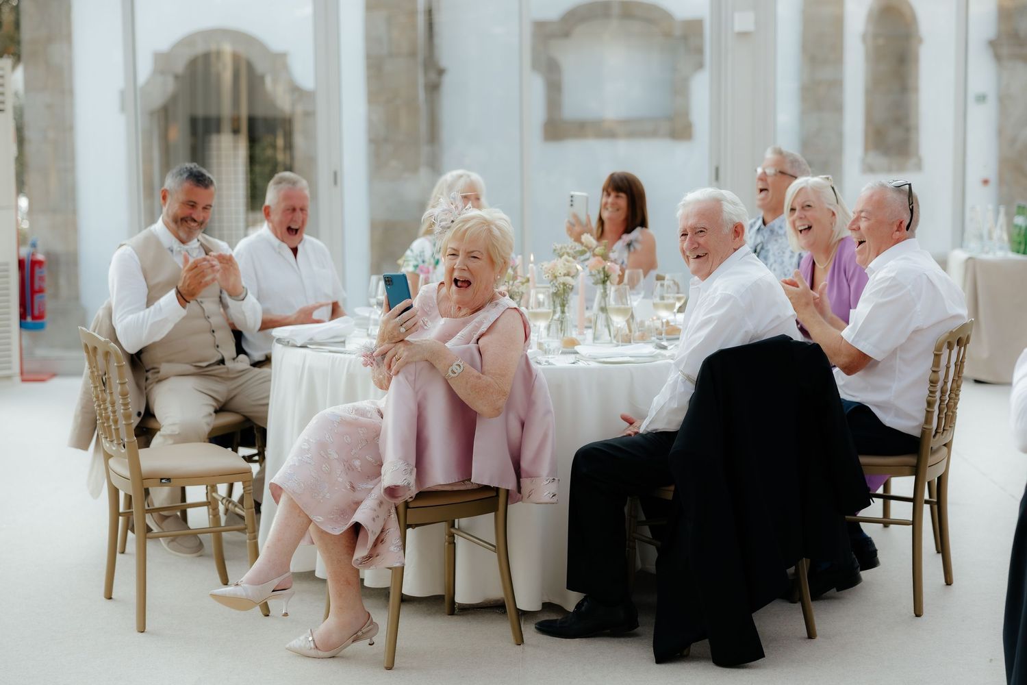 People in white attire seated at tables in an elegant white dining room during a formal gathering.
