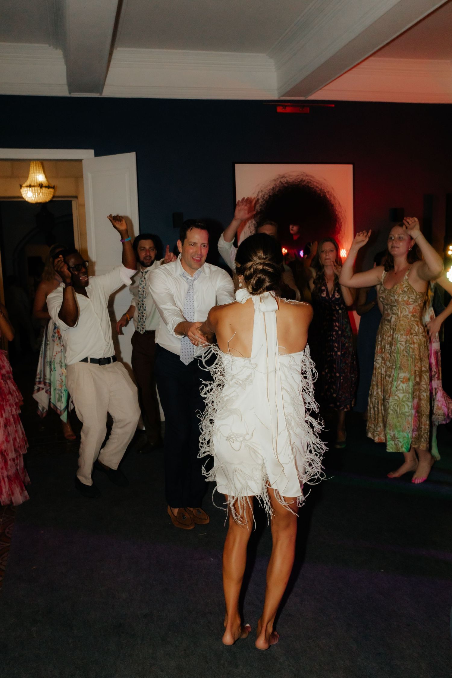 Wedding guests dance and celebrate on a crowded dance floor with festive lighting.