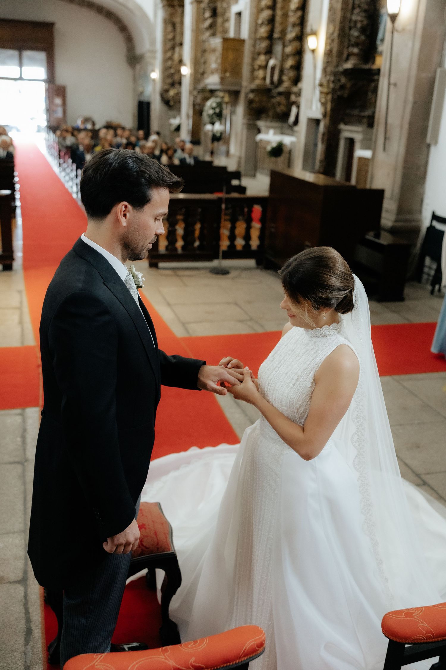 Bride places wedding ring on grooms hand during church ceremony with ornate interior.