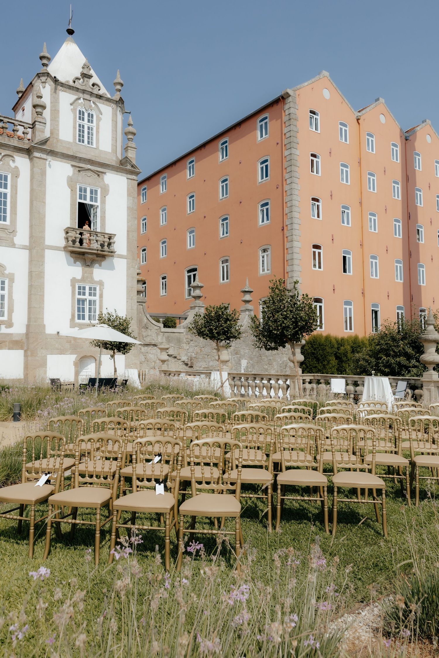 Gold Chiavari chairs arranged on green lawn before a grand historic palace for an outdoor wedding.