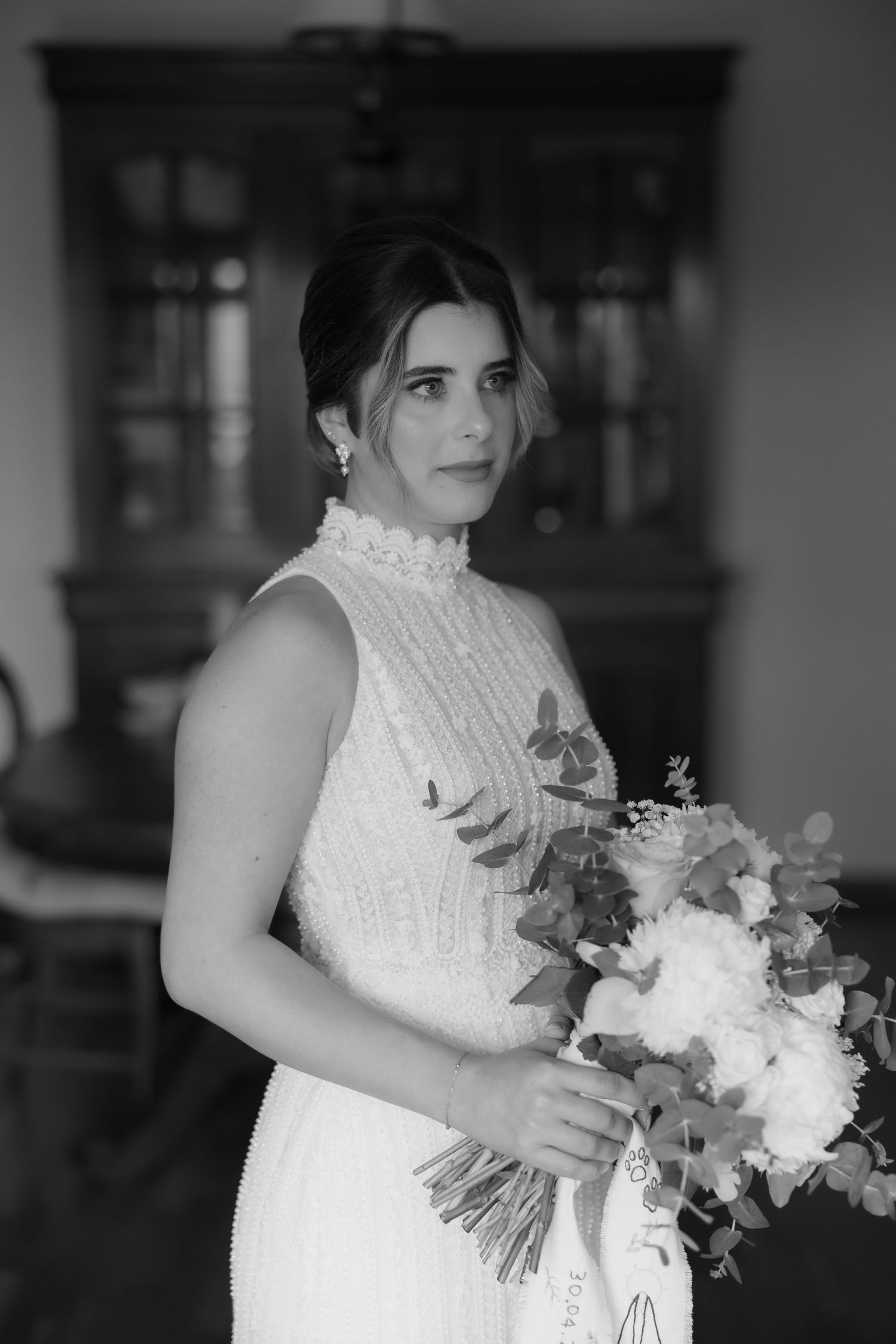 Black and white portrait of an elegant bride holding a white floral bouquet in a beaded gown.