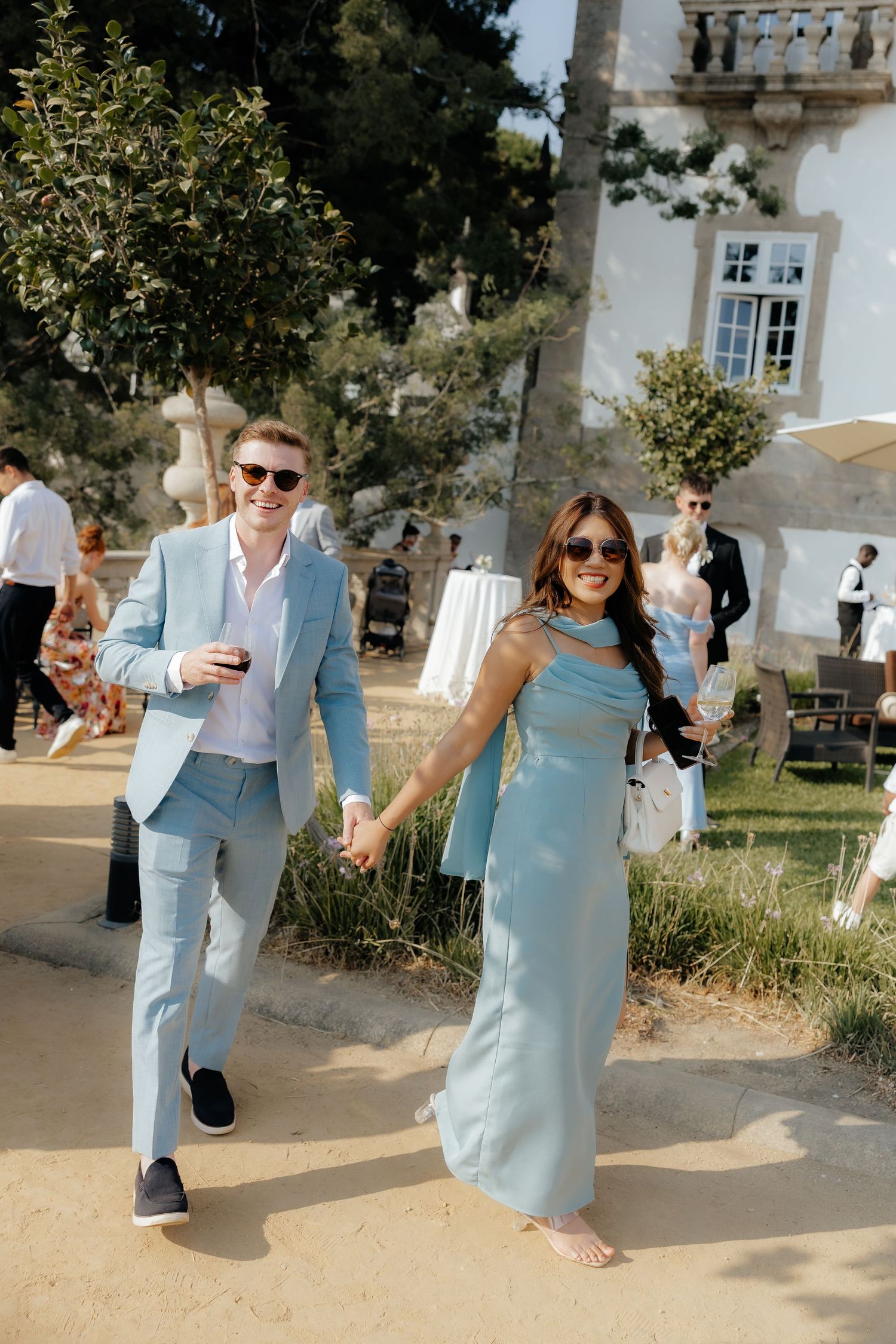 A couple in light blue attire walking together at an outdoor event with a historic building in the background.