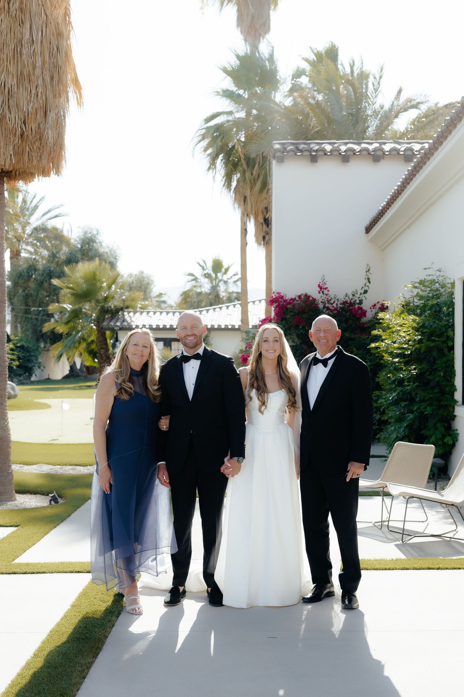 Bride and groom posing with family members in formal attire at an outdoor wedding venue.