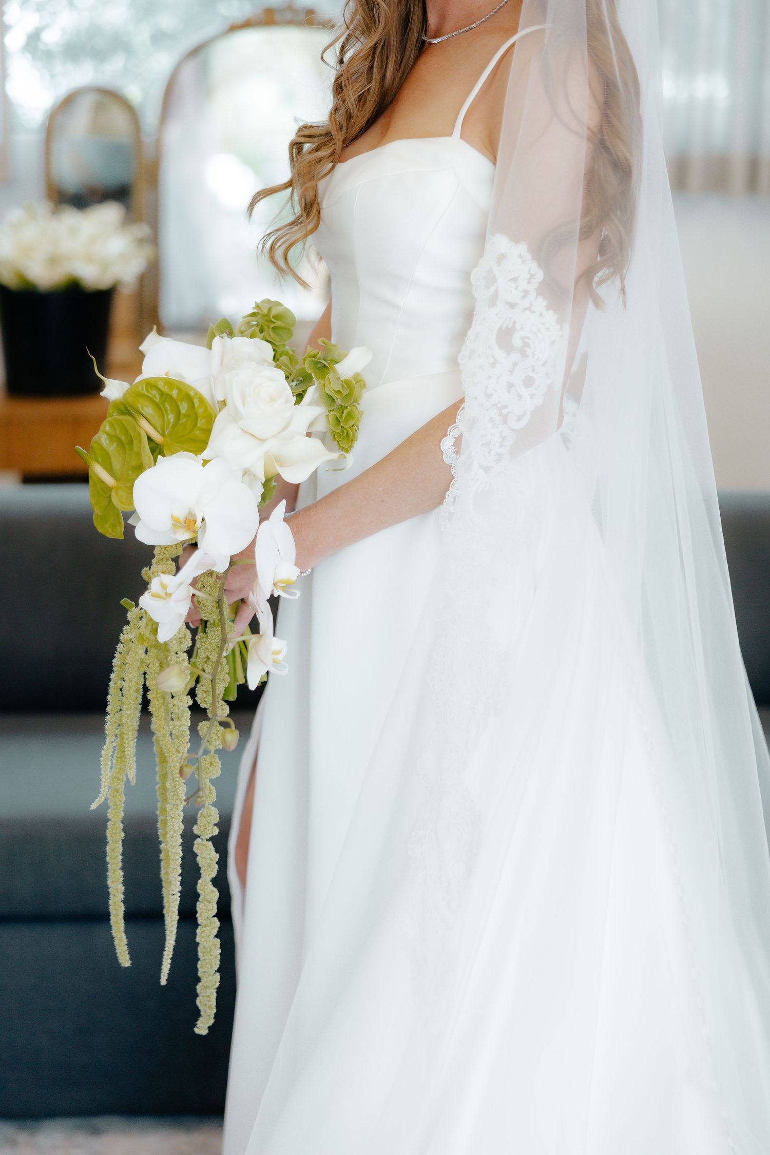 Bride holding a cascading bouquet of white orchids and green anthurium flowers.