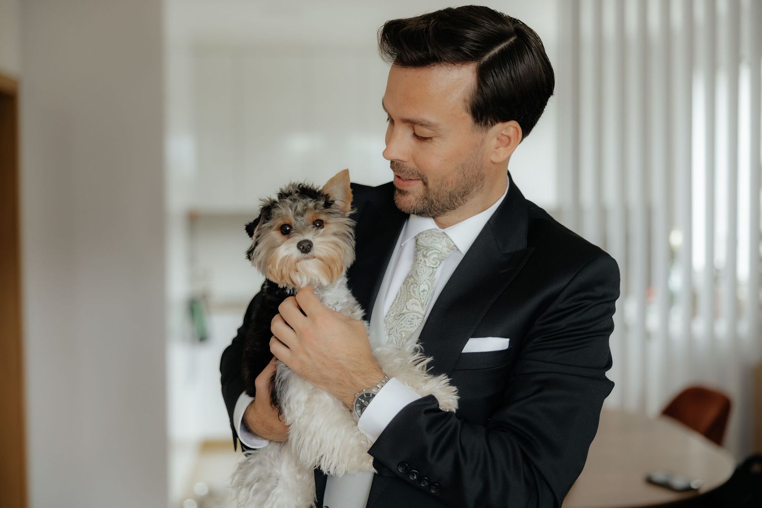 Smiling groom in black tuxedo cradles a small Yorkshire Terrier dog.