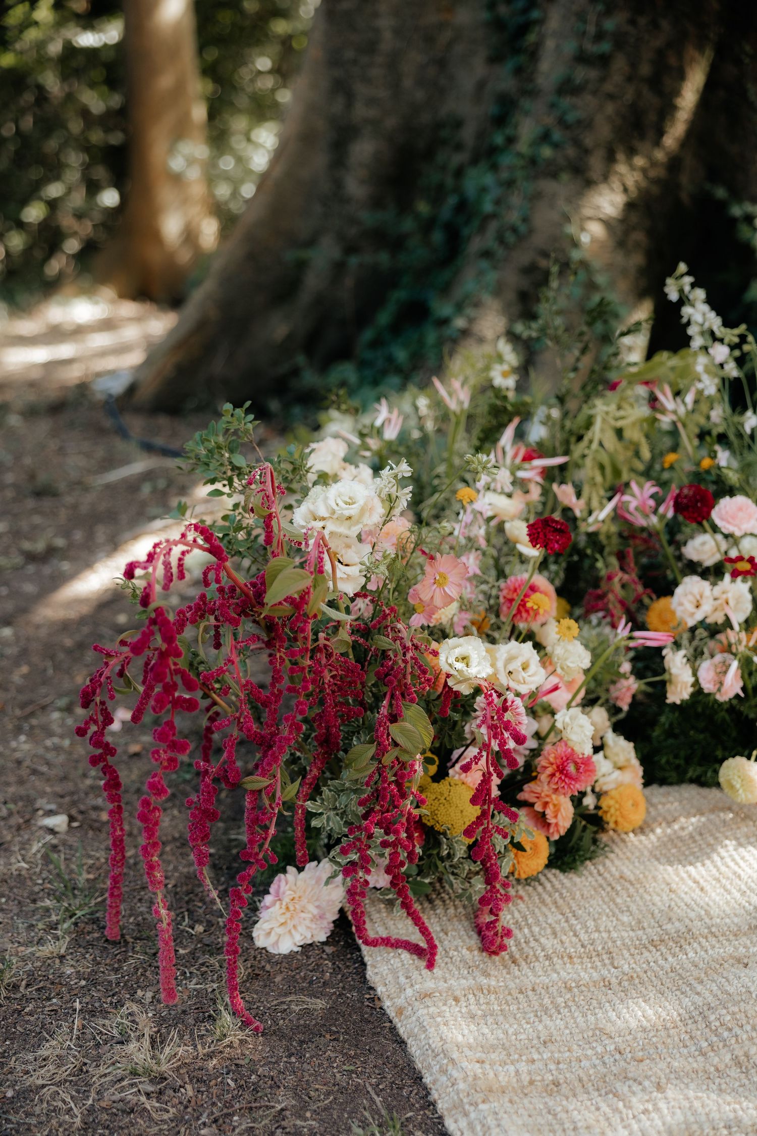 Colorful floral arrangement with pink amaranth and roses laid on ground in outdoor setting.