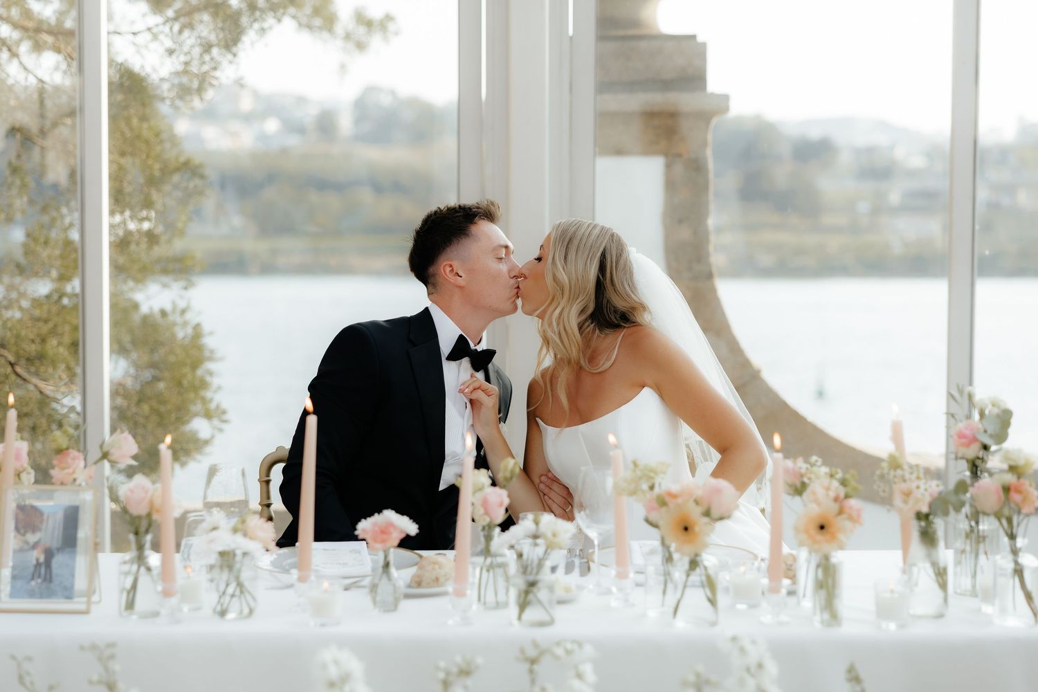 Romantic couple sharing a tender kiss during their outdoor waterfront wedding ceremony at sunset.