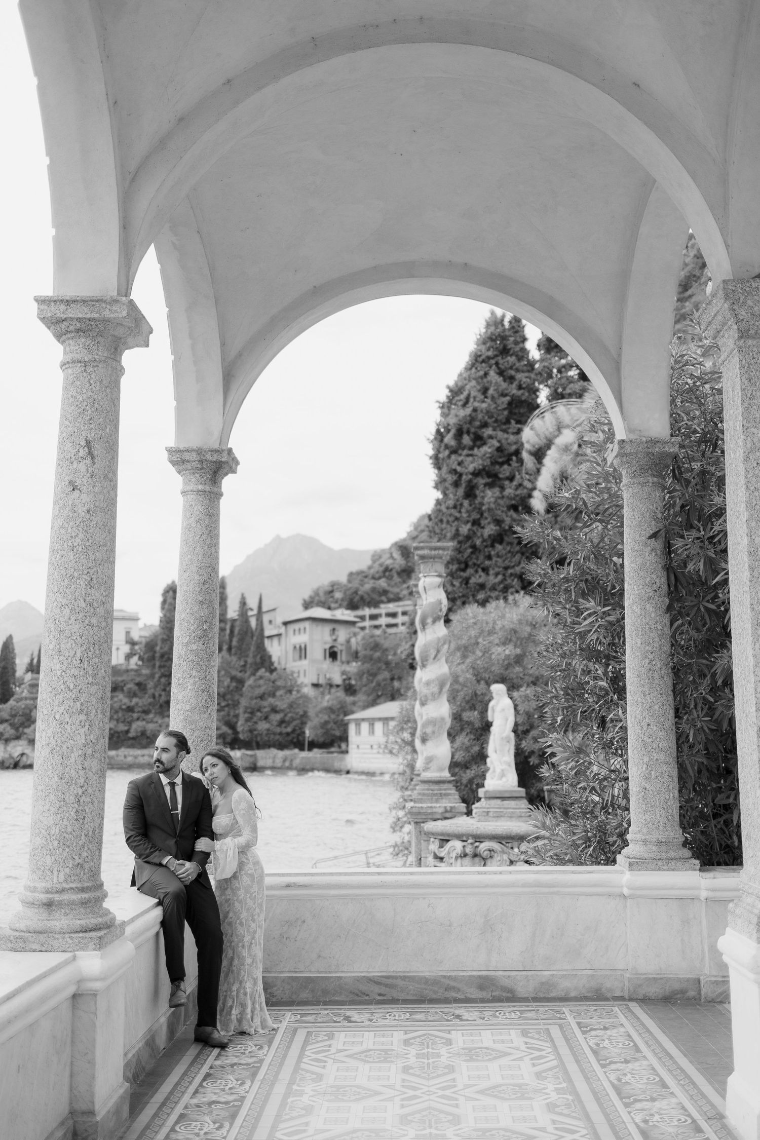 Black and white photo of couple embracing under marble arches at an Italian lakeside villa.