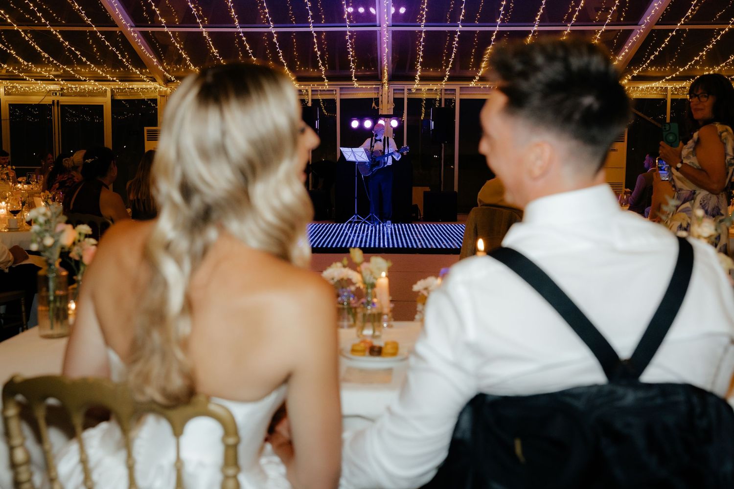 Wedding guests dance and celebrate on a dimly lit dance floor decorated with string lights during an evening reception.